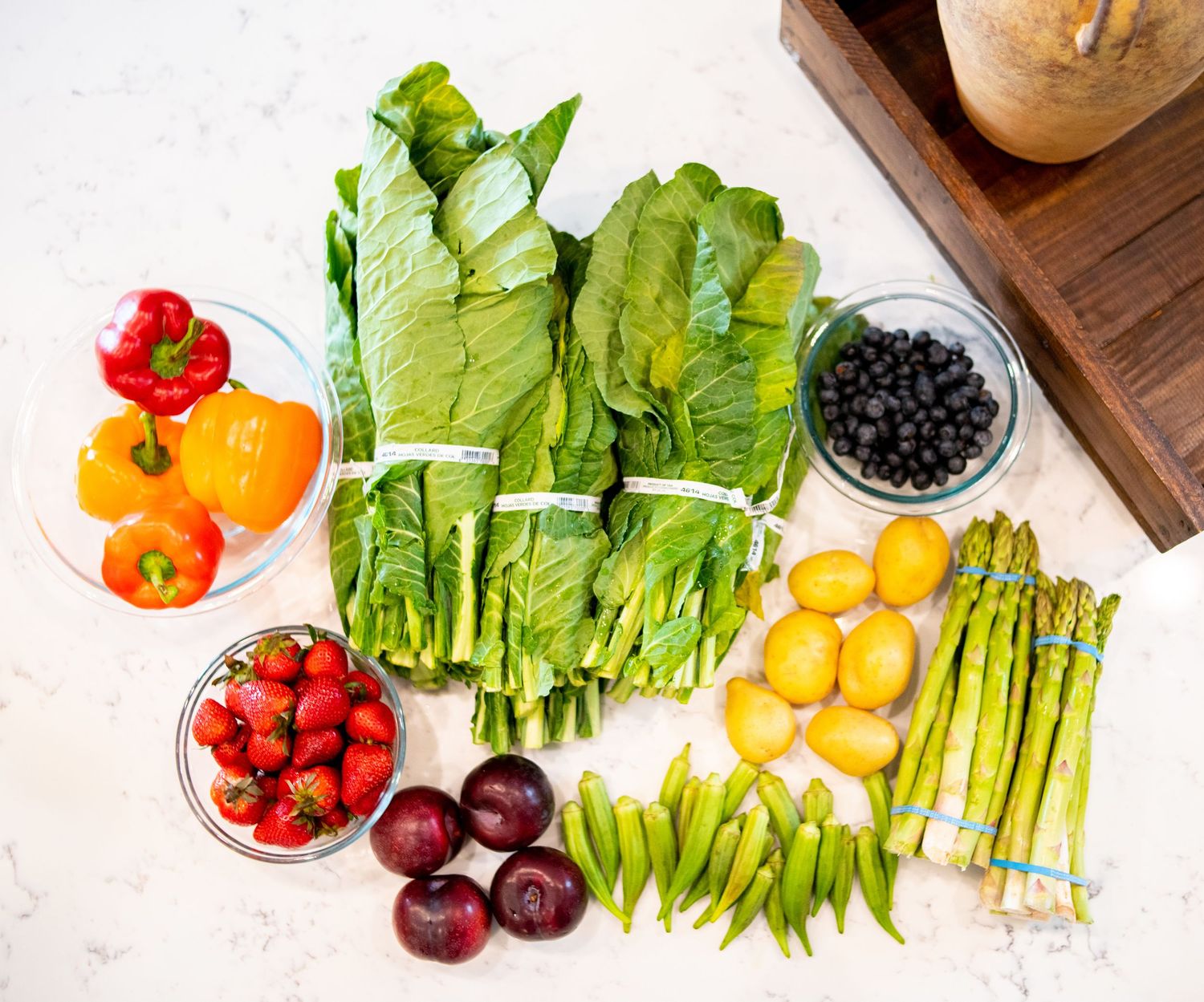 Fresh colorful produce and vegetables arranged in a line on white marble countertop.