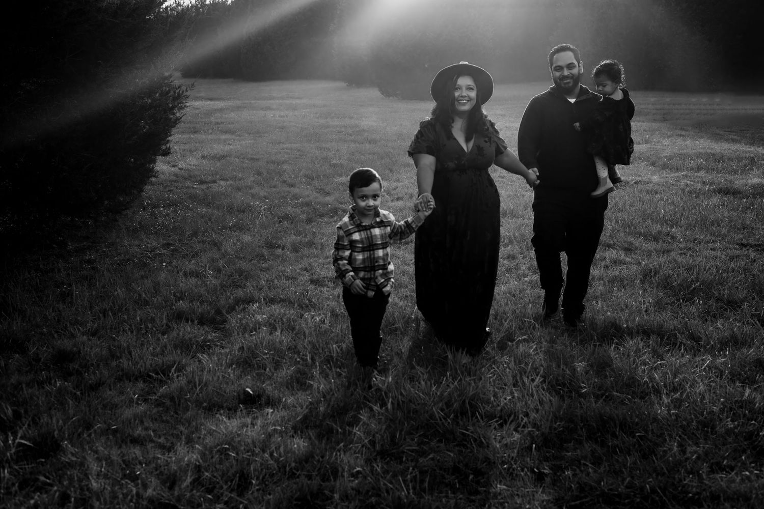 A family walks together through a misty field at sunset creating a moody black and white silhouette.
