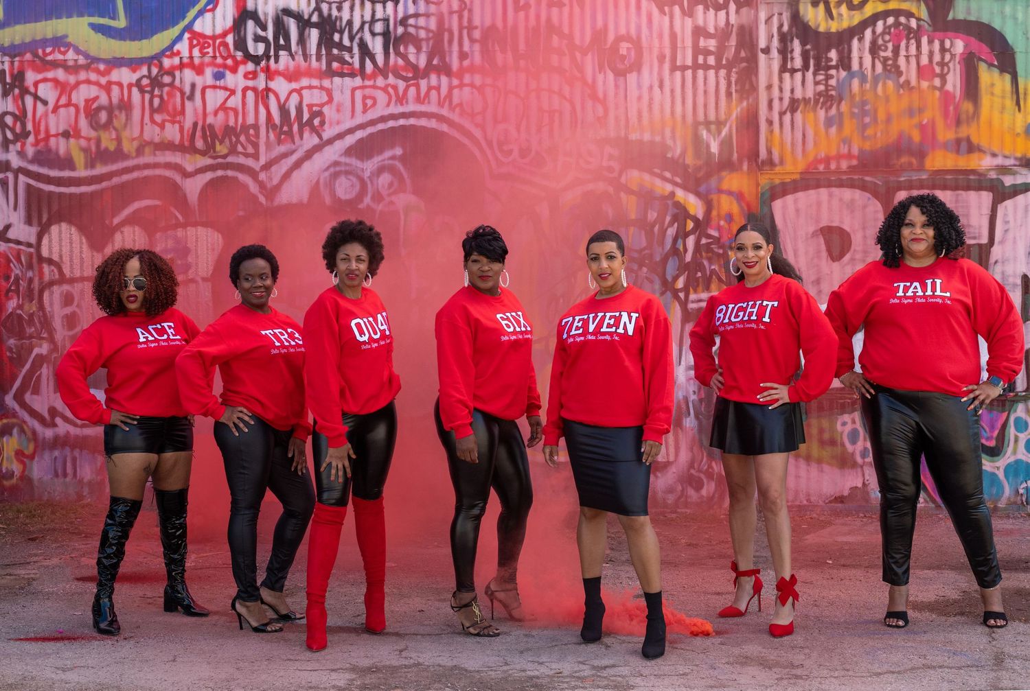 Dance performance lineup with people in red shirts and black pants against vibrant street art wall.