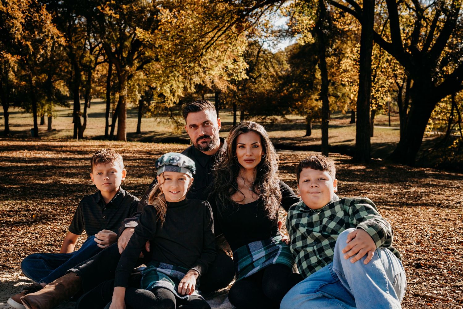 A family sits together on fallen autumn leaves in a park setting.