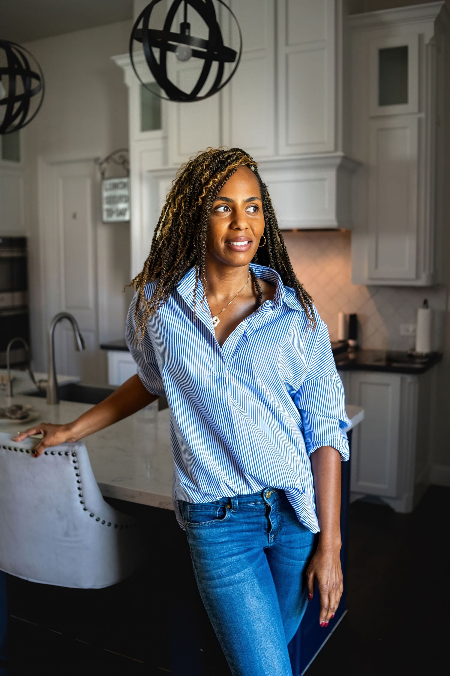 Person in blue button-down shirt and jeans dancing joyfully in bright white kitchen.