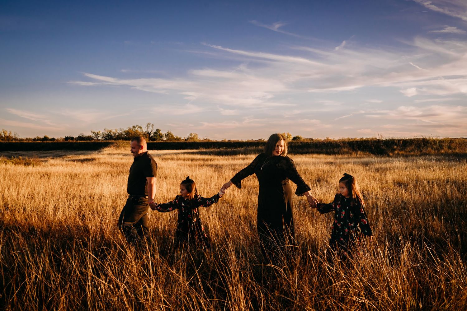 Silhouettes of people walking through golden wheat field at sunset.