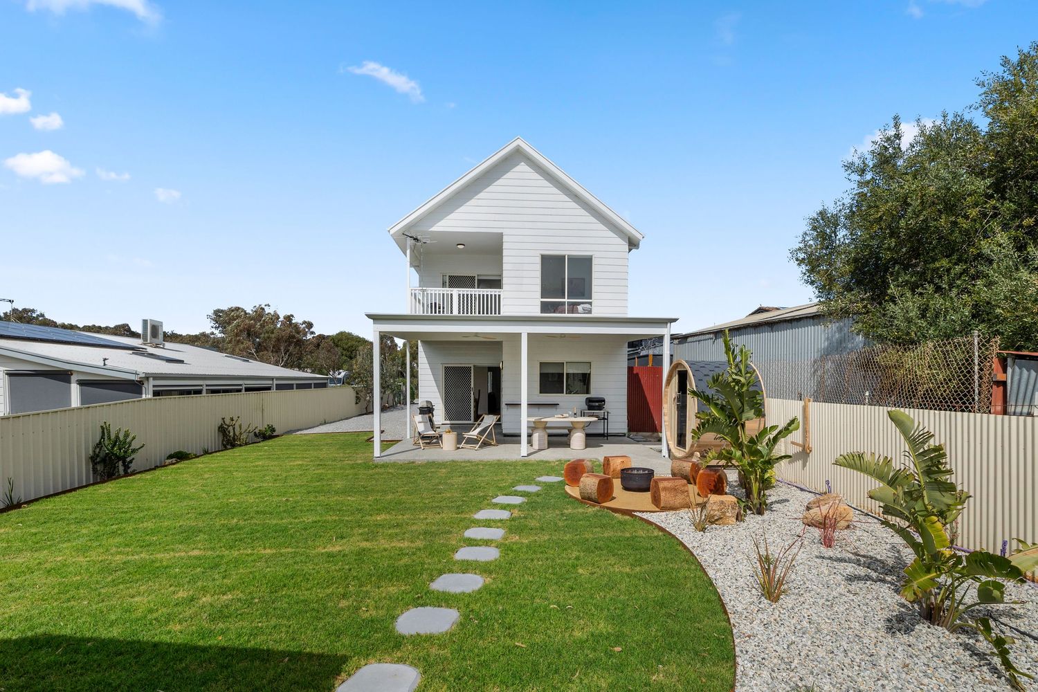 Real Estate Photograph Modern white two-story coastal home with manicured lawn, paved walkway and beach-inspired landscaping design.