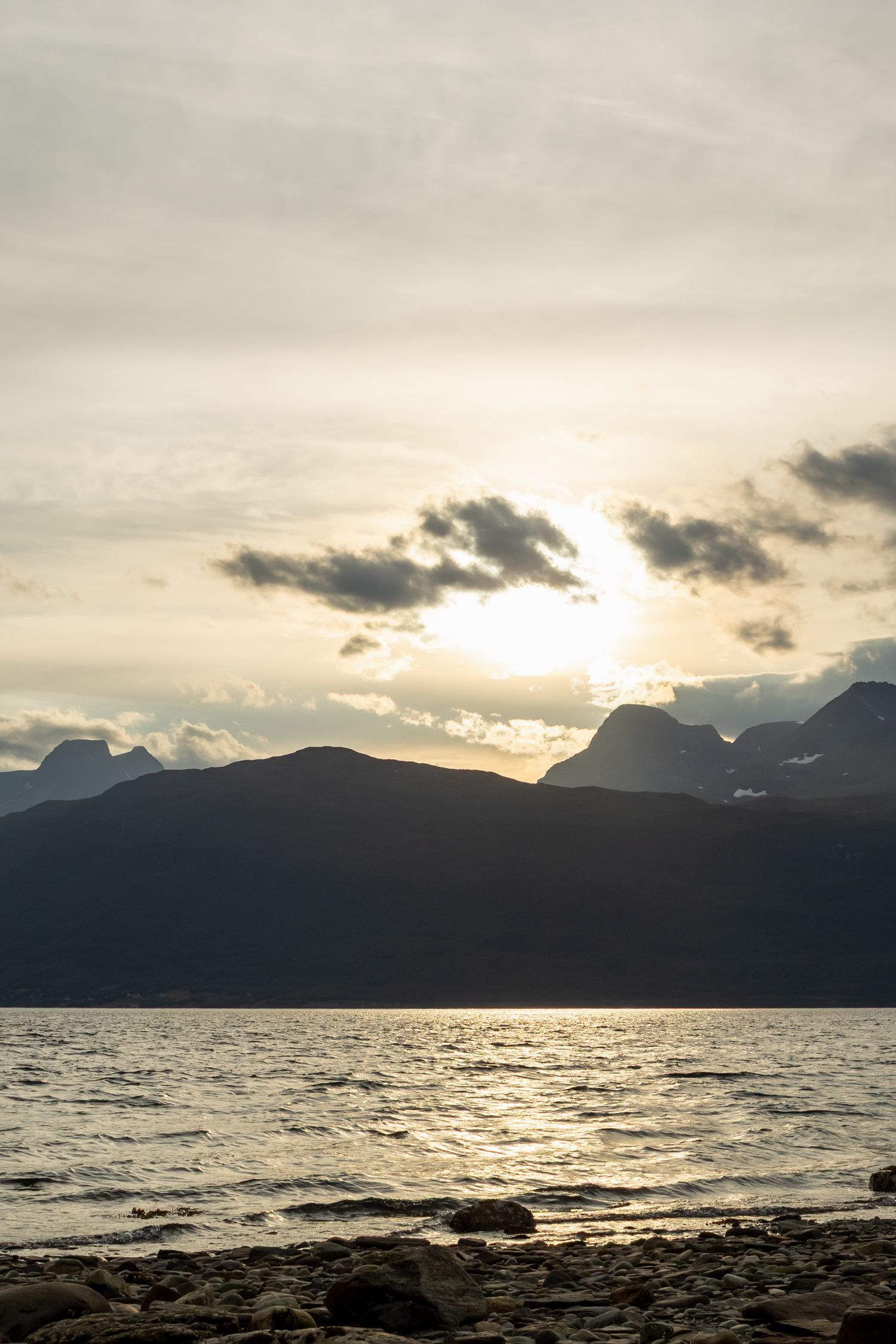 Dramatic sunset over mountain lake with silhouetted peaks and rocky shore.