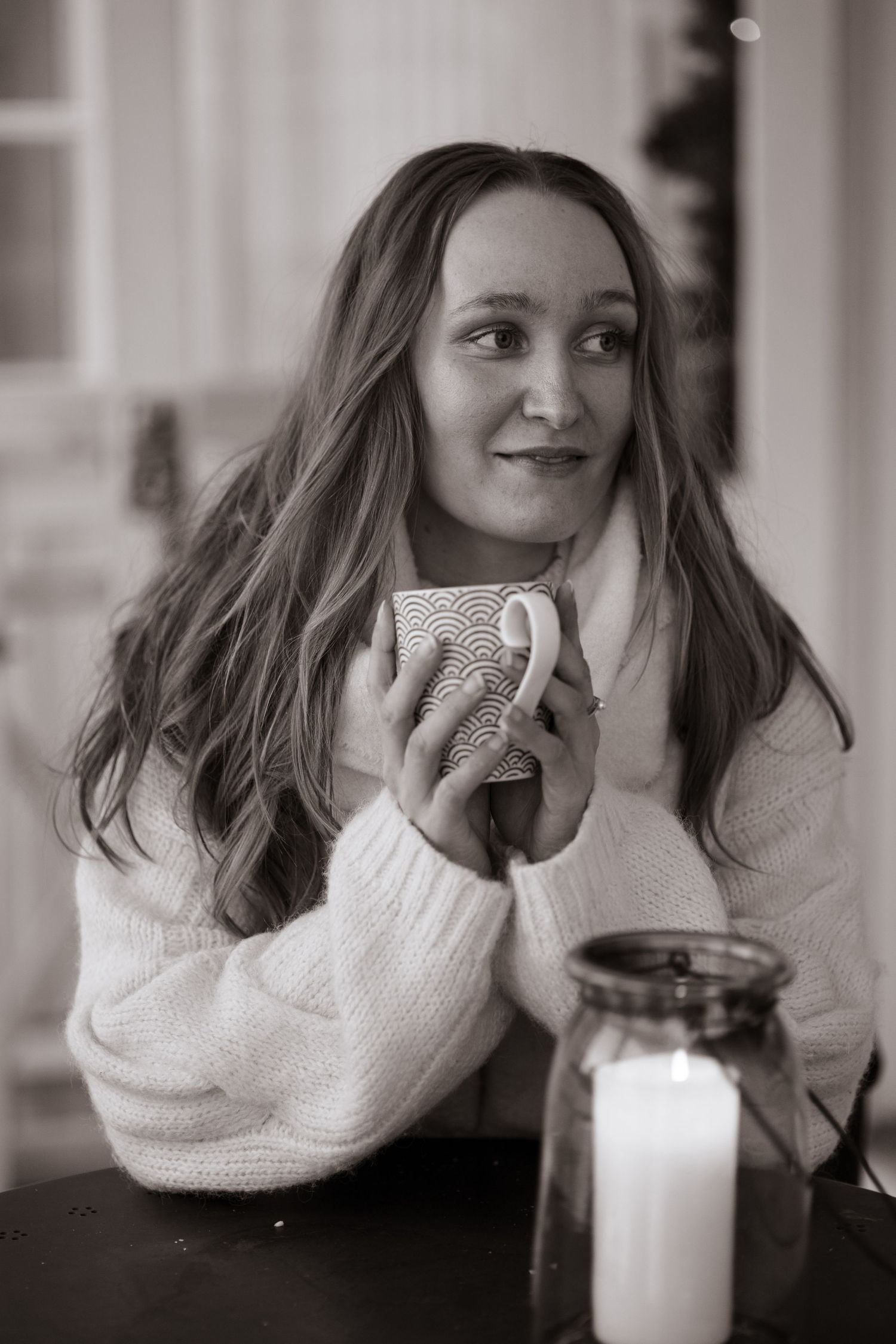 Black and white portrait of someone holding a mug near a lit candle.