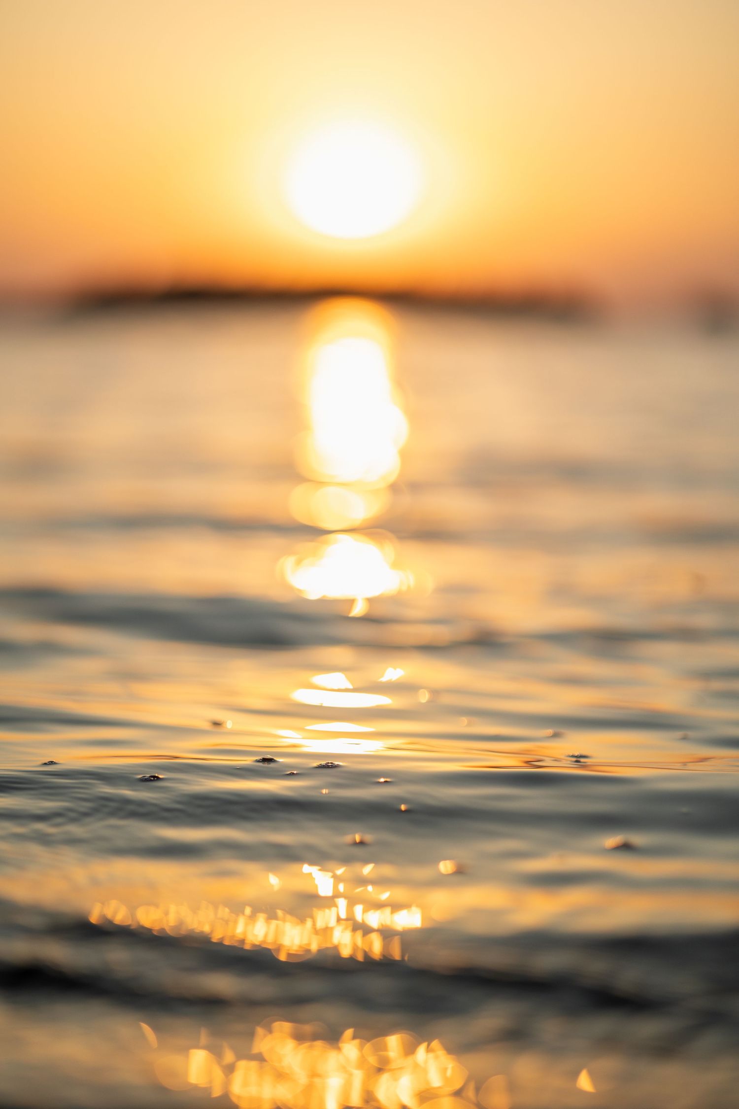 Golden sunlight reflects off rippling ocean waves during a serene sunset creating a dreamy water surface.