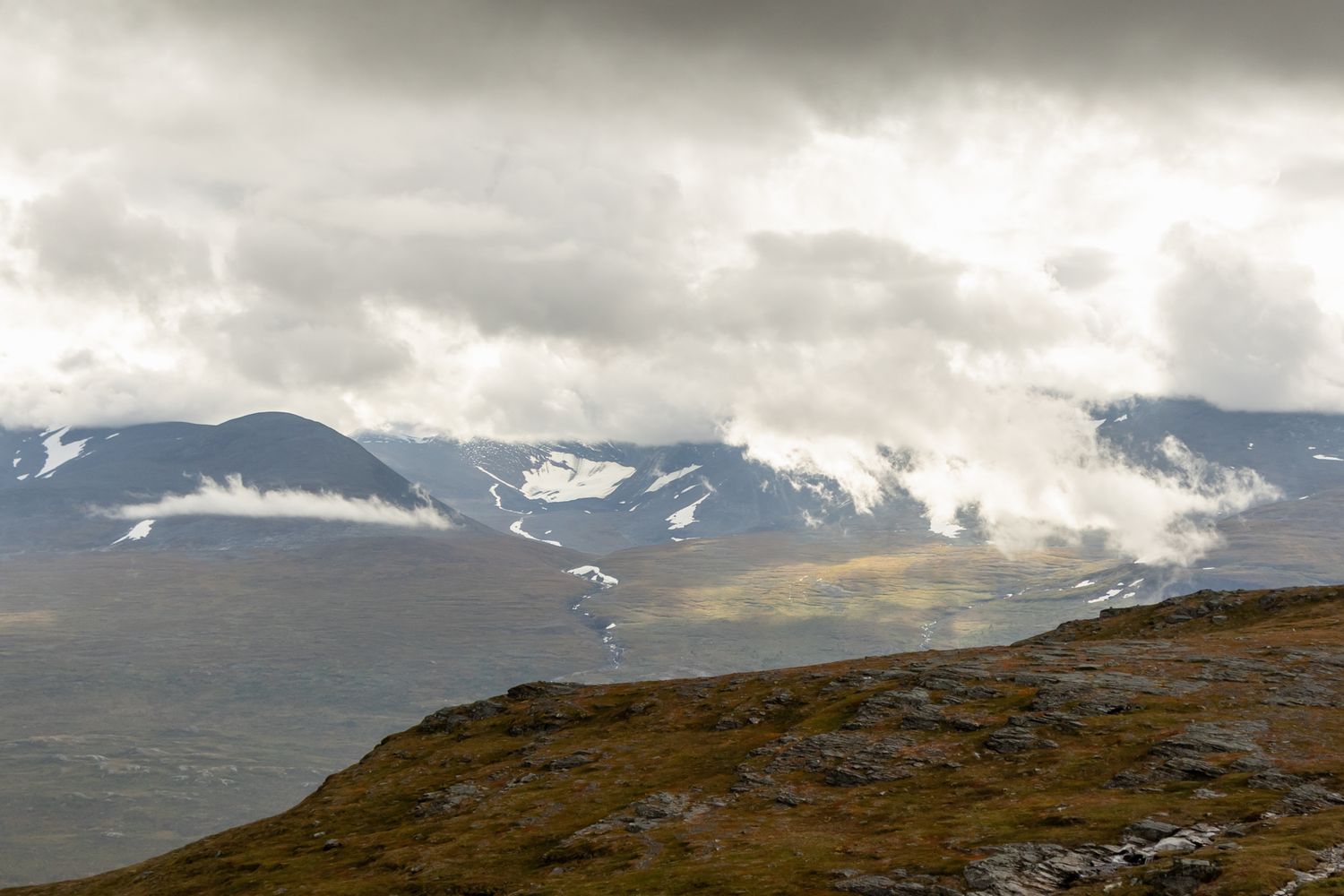 Dramatic mountain range with snow patches under moody overcast skies.