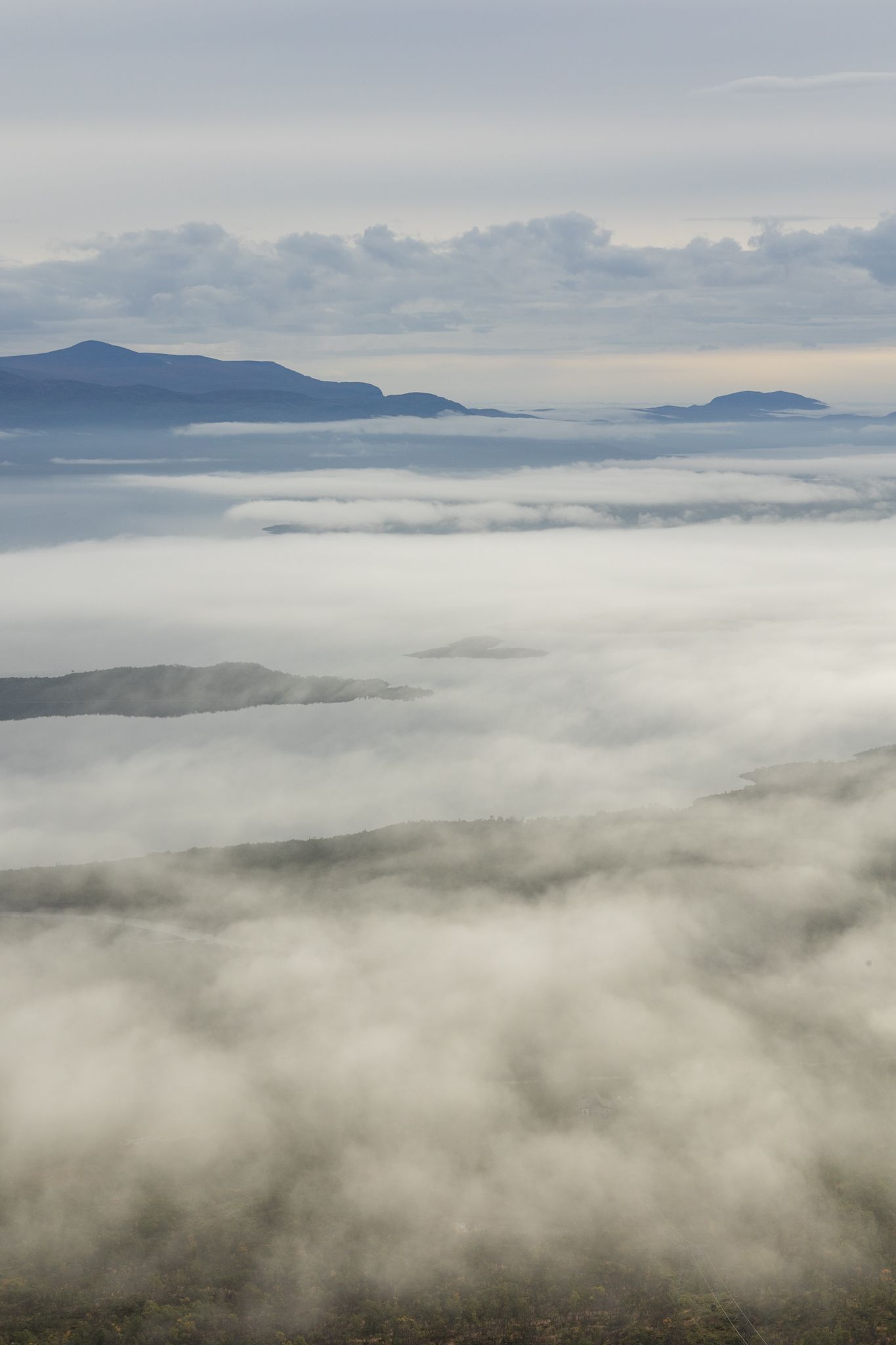 Rolling sea of clouds blankets a valley with mountain peaks emerging in the distance.