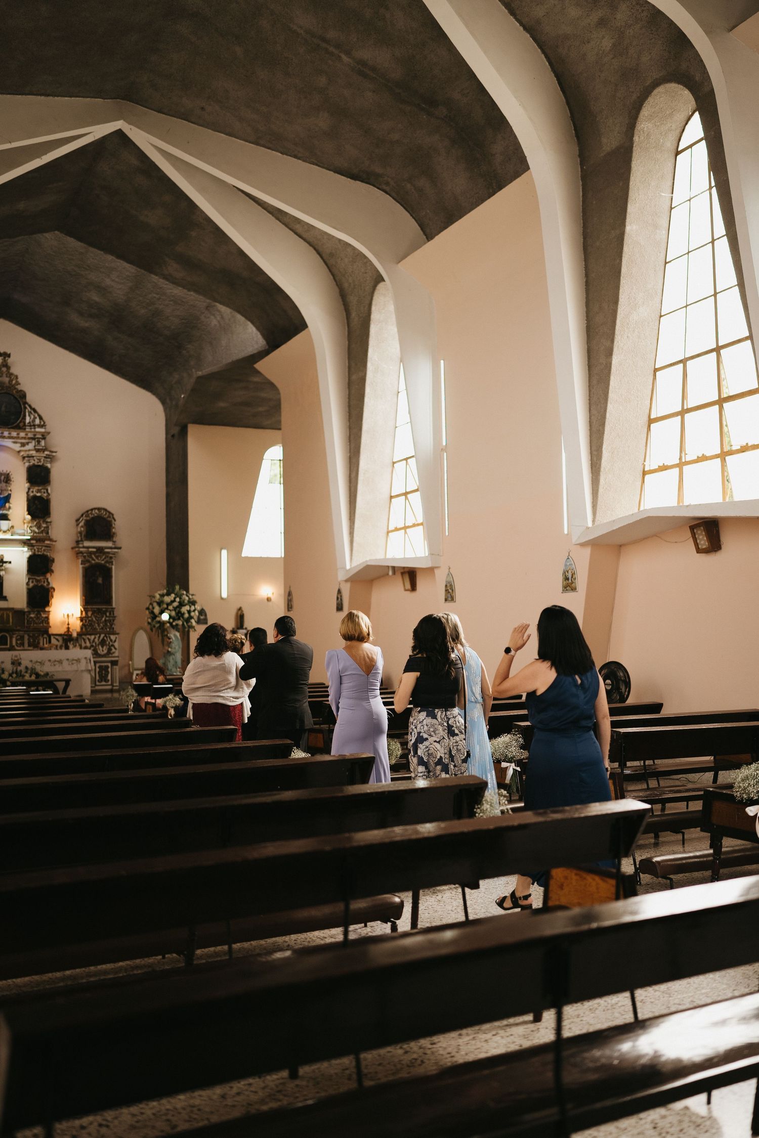 Interior of a church with arched windows and wooden pews bathed in natural light.