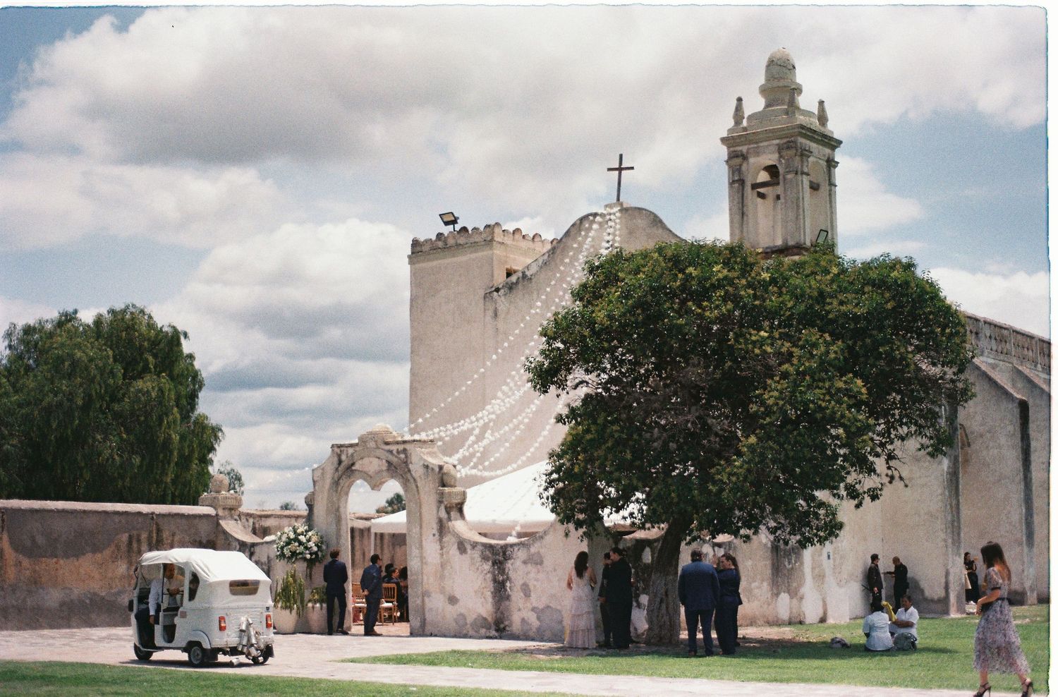 Historic church exterior with bell tower and trees under cloudy sky.