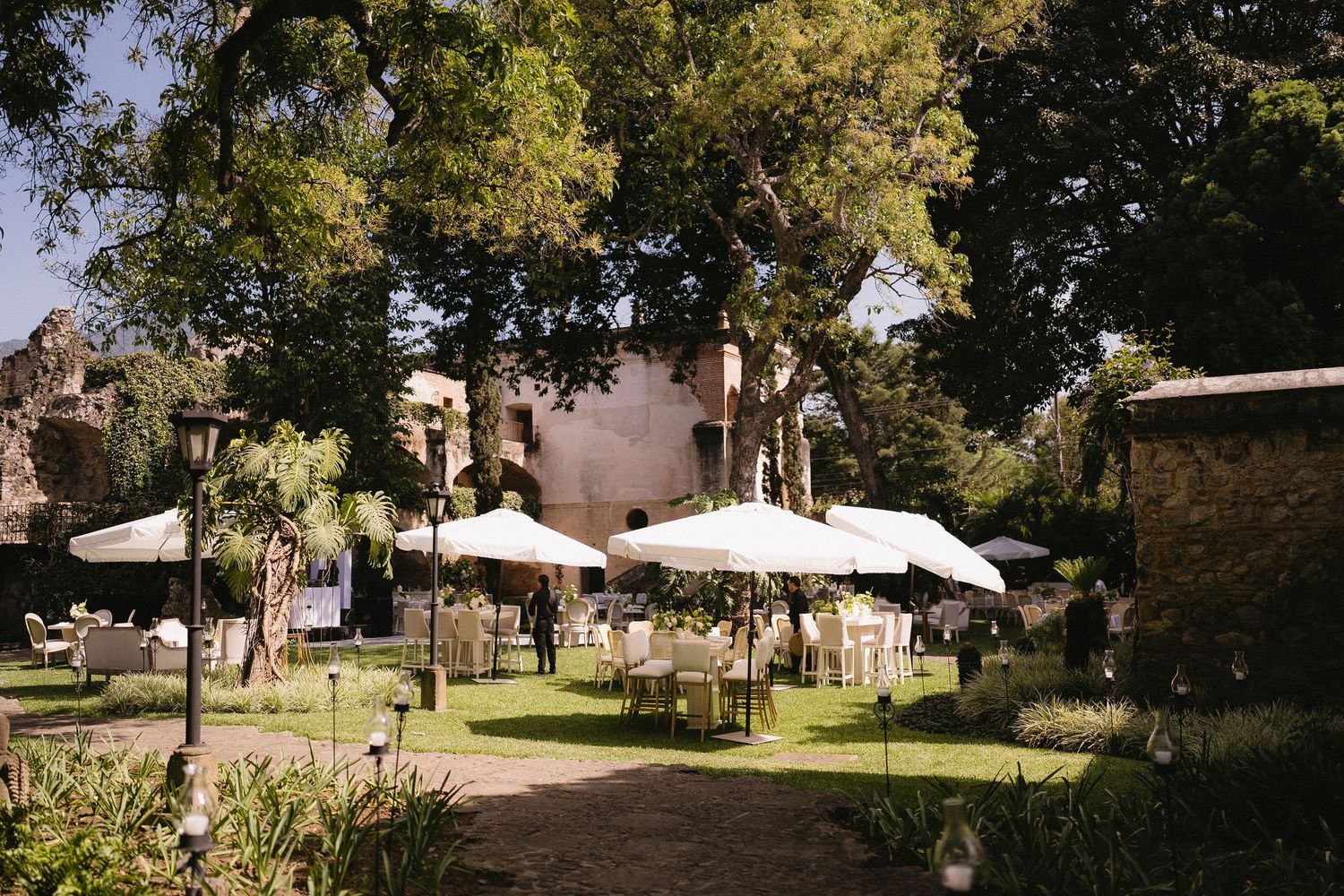 Panoramic view of a garden venue with white umbrellas and trees.