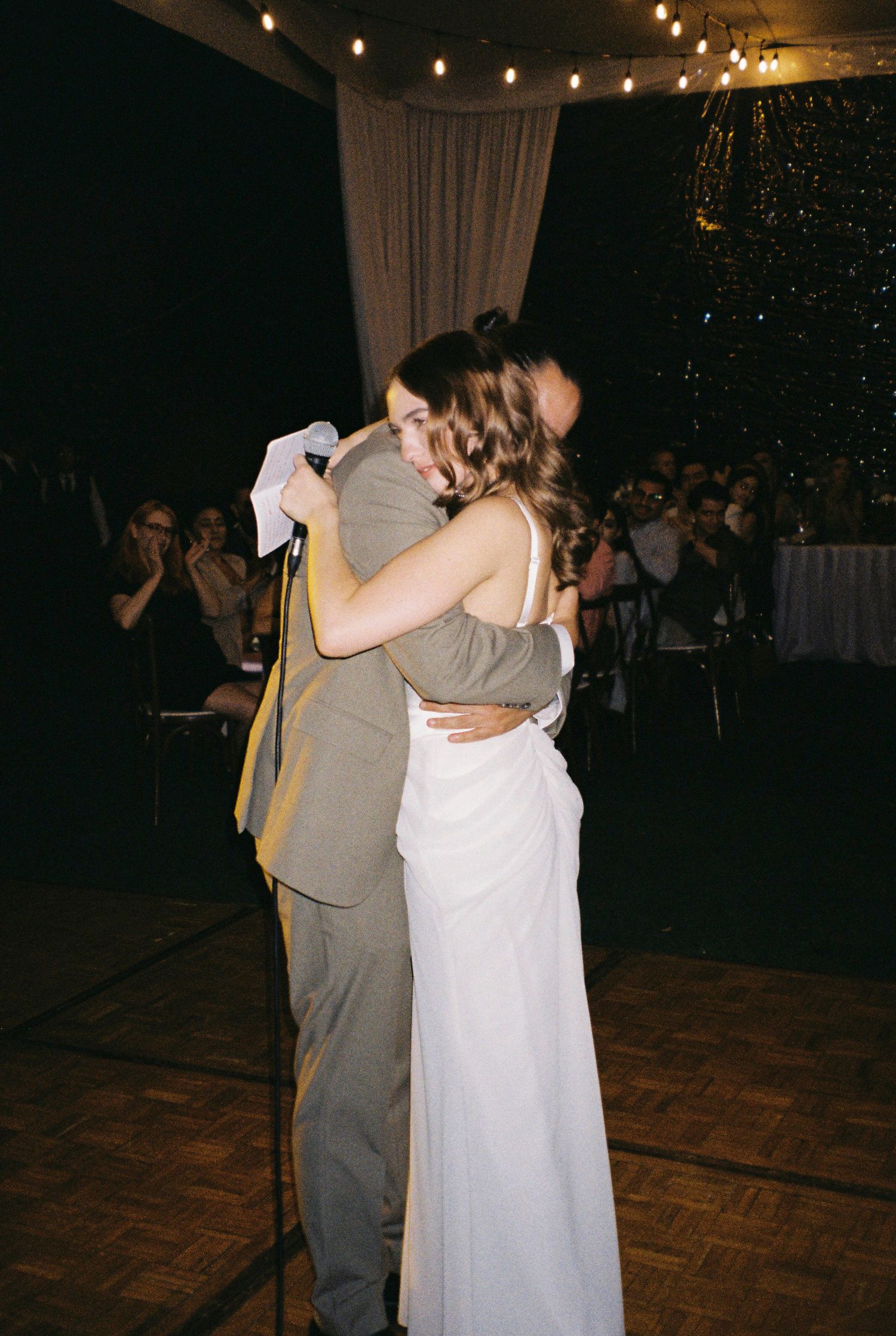 Couple dancing together at a wedding reception under string lights.
