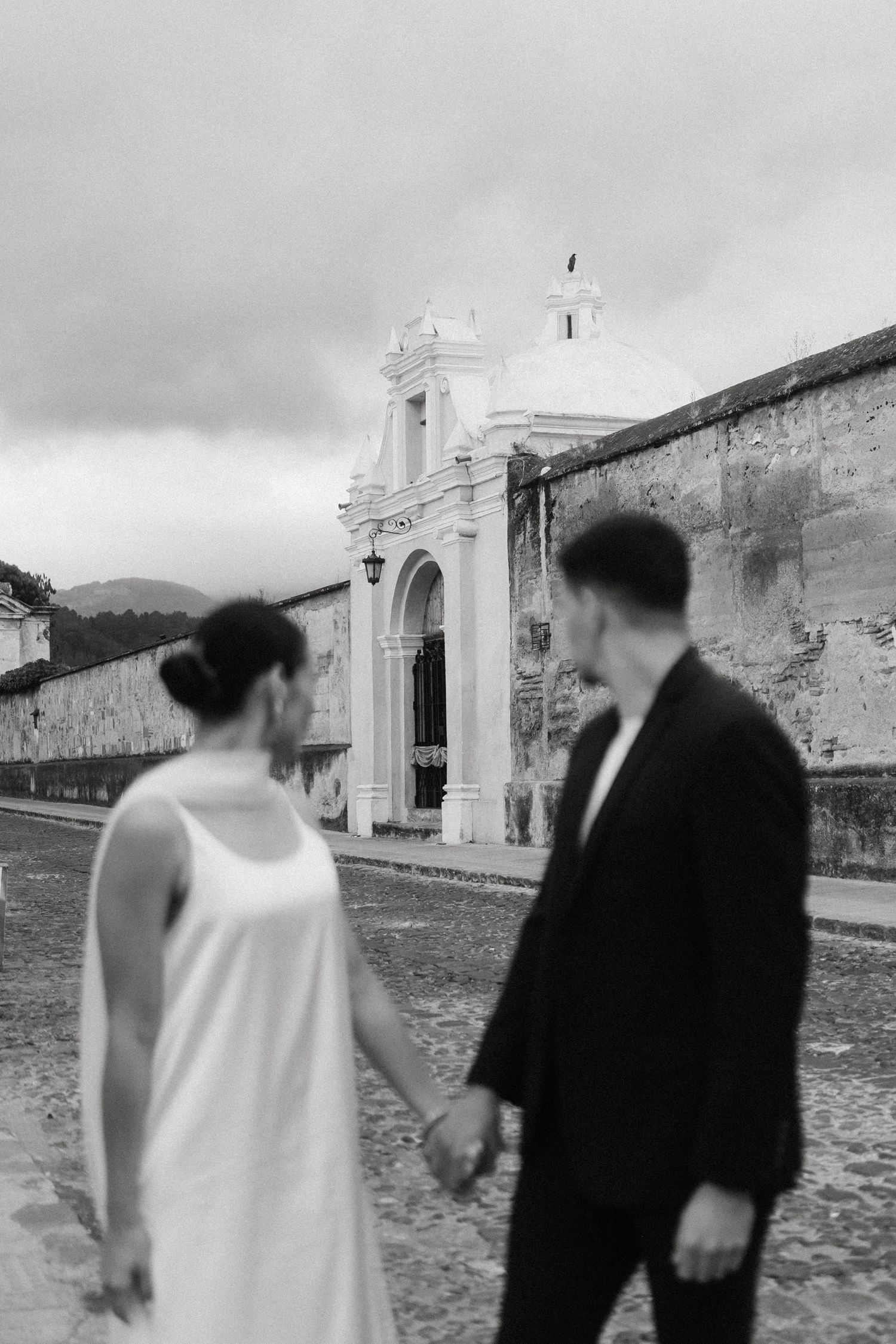 Black and white photo of a couple walking near historic stone buildings.
