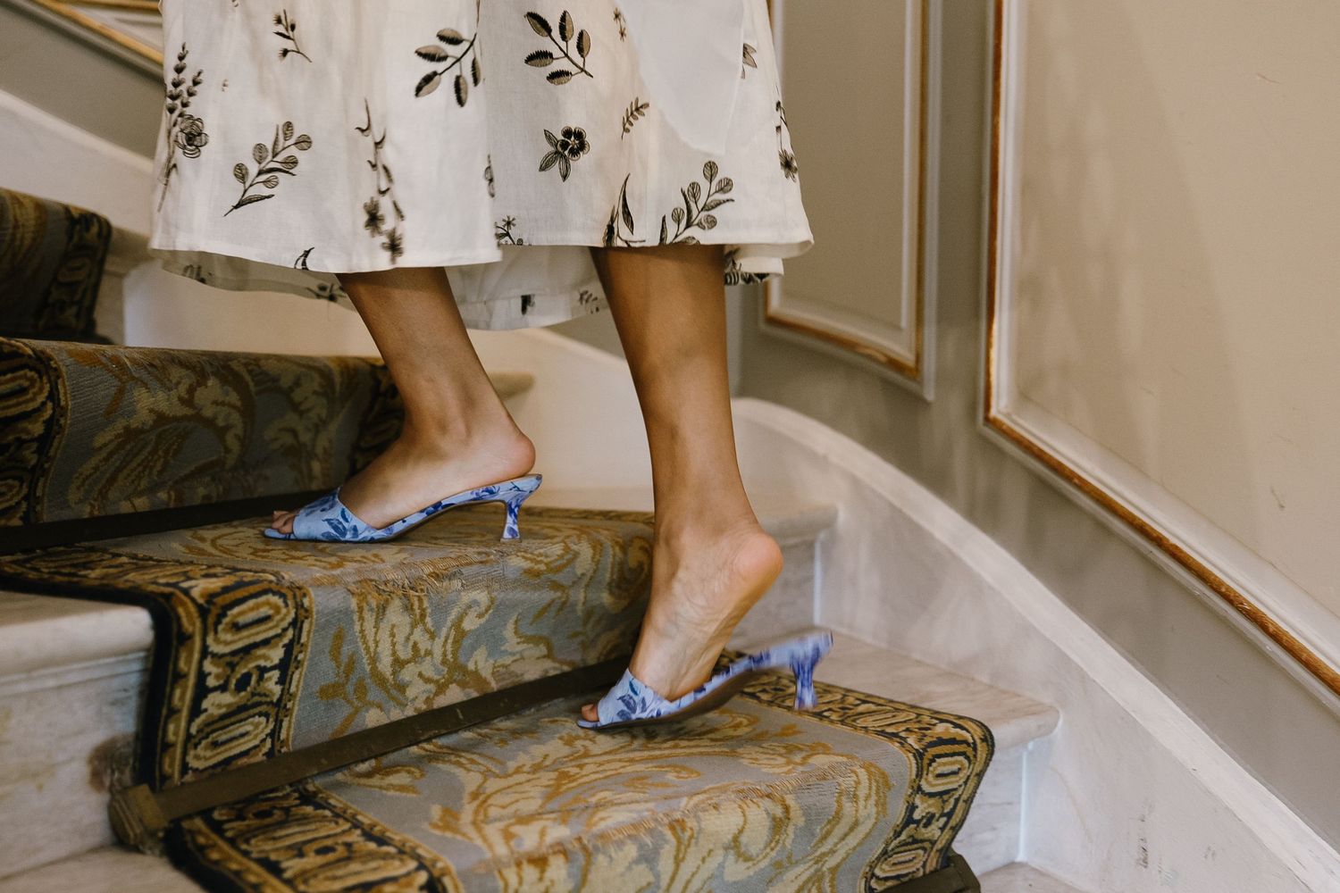 Close-up of blue shoes walking on an ornate carpet with floral patterns.