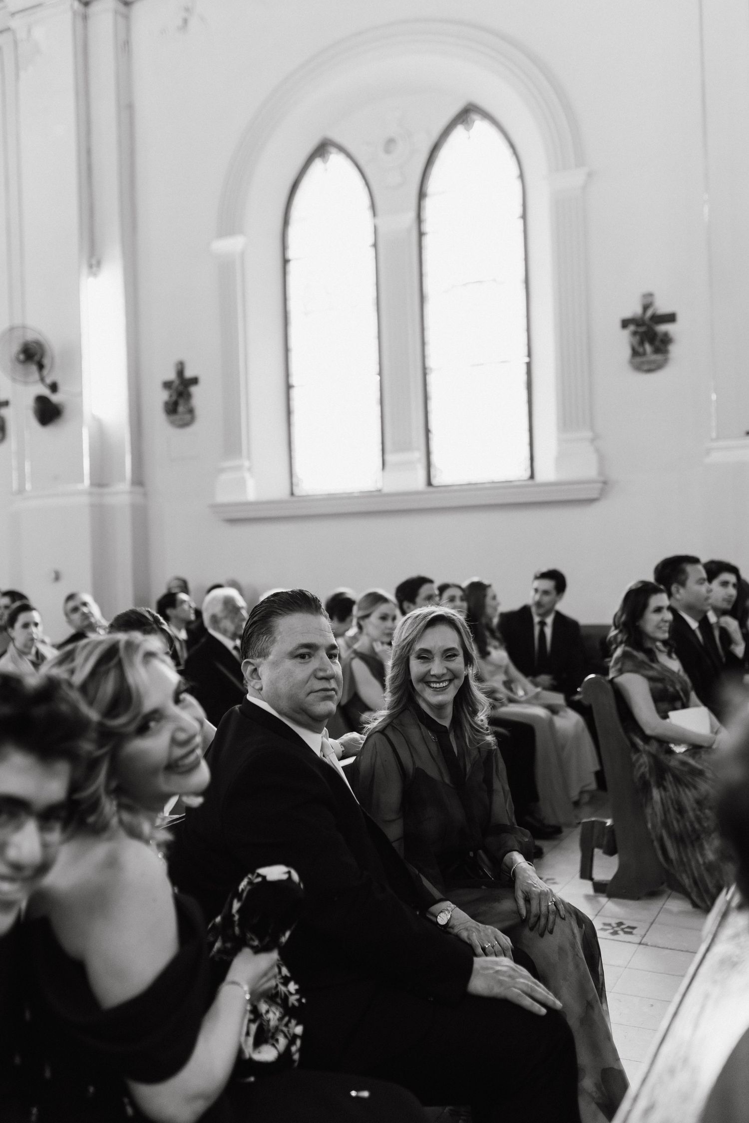 Church interior filled with wedding guests seated in pews under arched windows.
