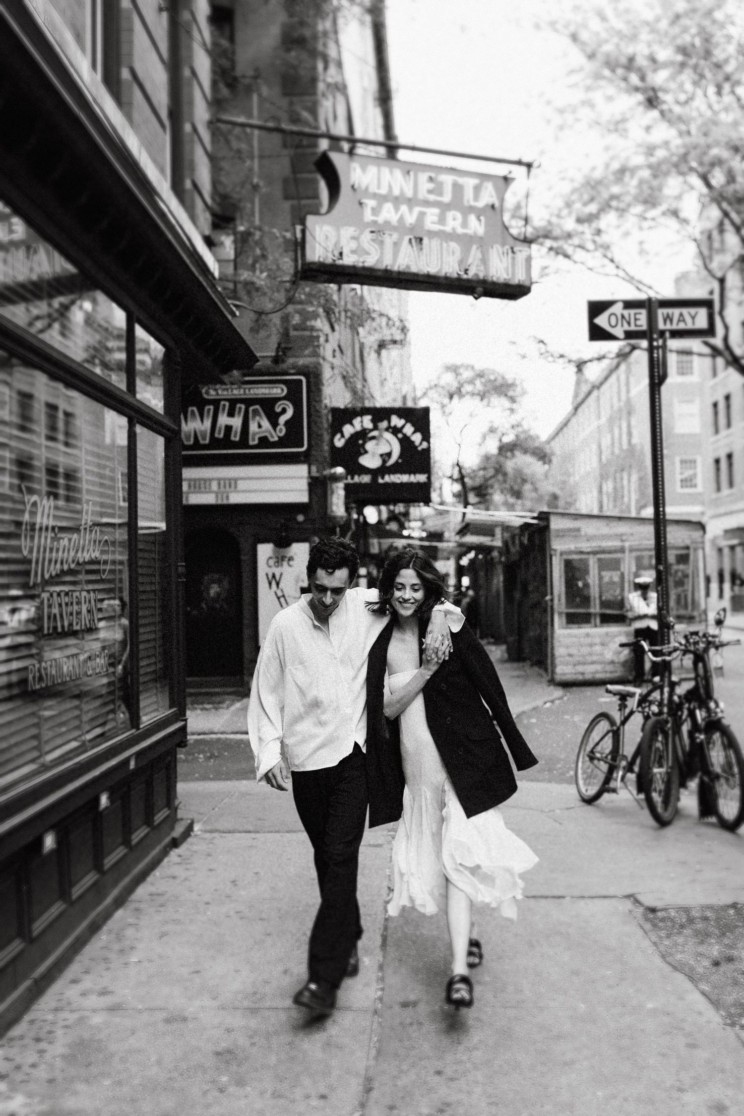 Black and white street photography of couple walking past city shops.