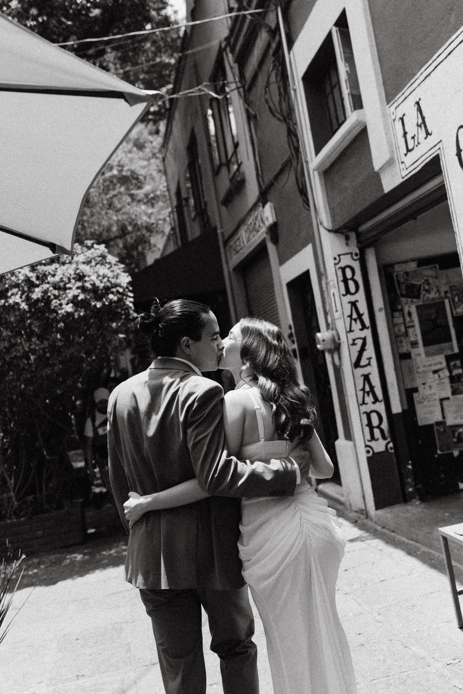 A couple walking away from camera down a city street with storefronts visible.