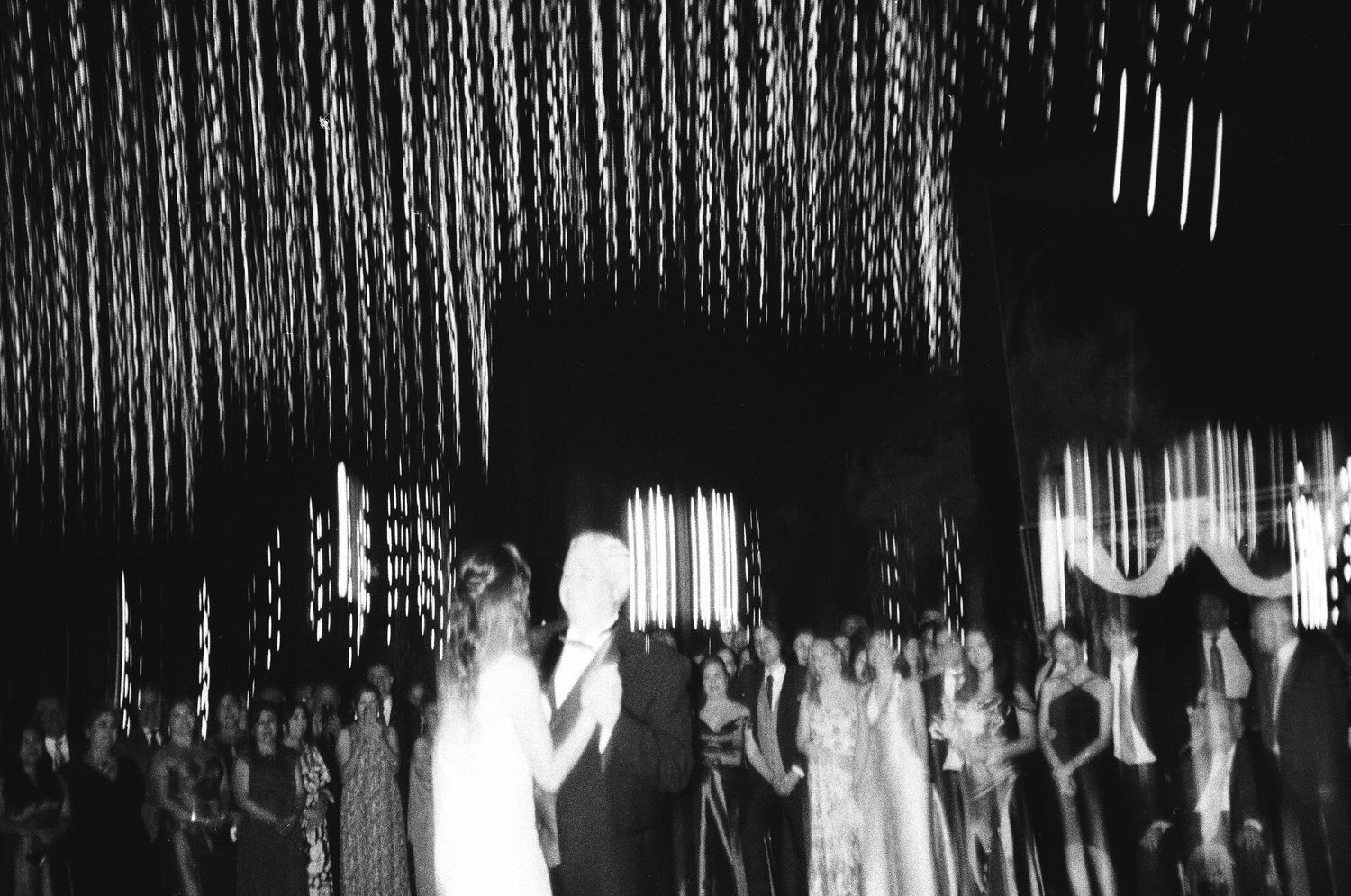 Abstract black and white photo showing hanging string lights or curtains creating vertical patterns.
