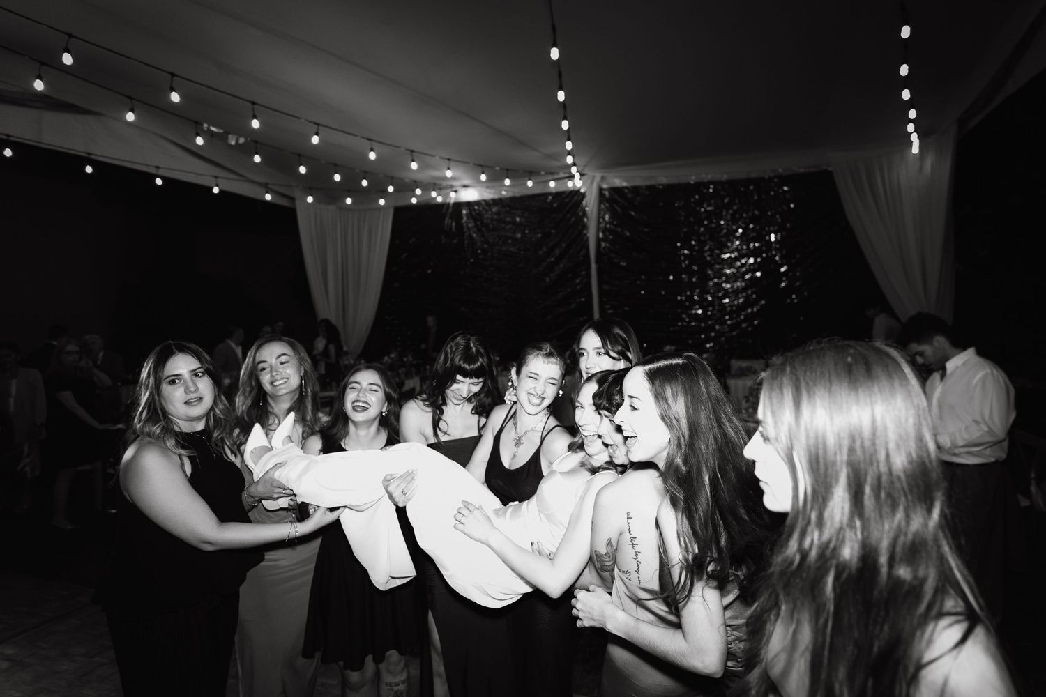Dance floor filled with silhouettes under string lights at an evening celebration.