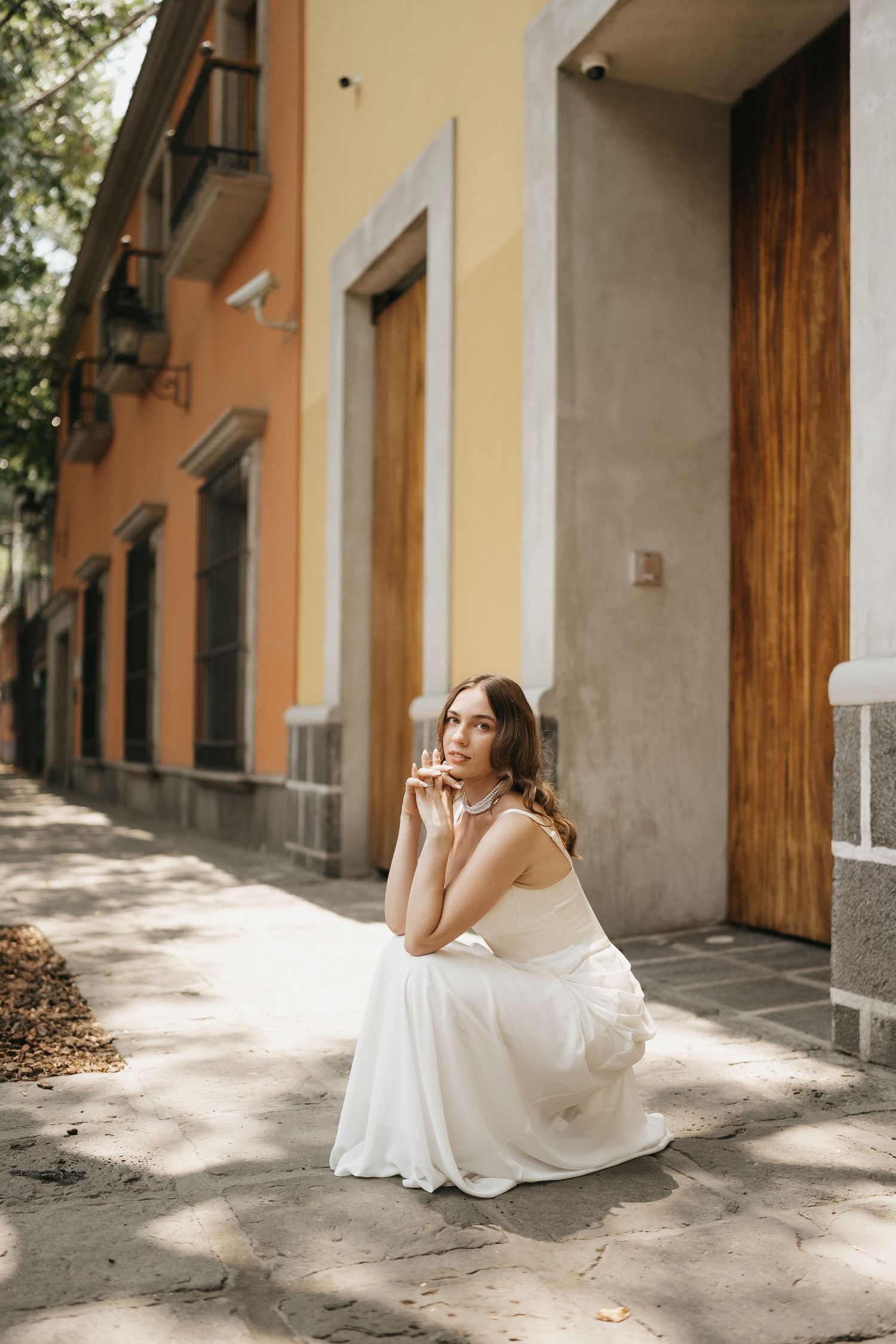 A white wedding dress flows elegantly in natural sunlight against a rustic building exterior.