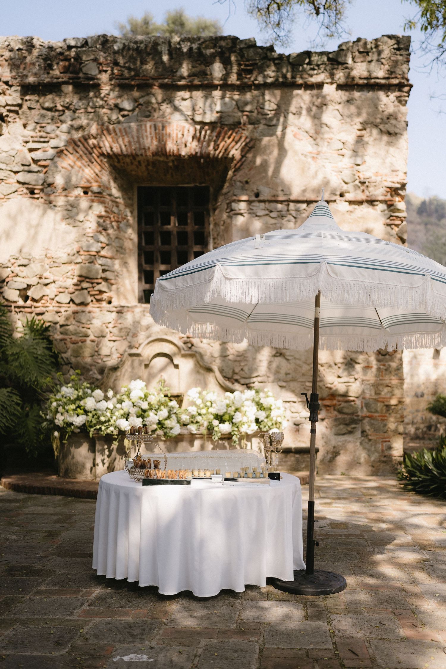 White umbrella-covered tables with floral arrangements set against a rustic stone wall.