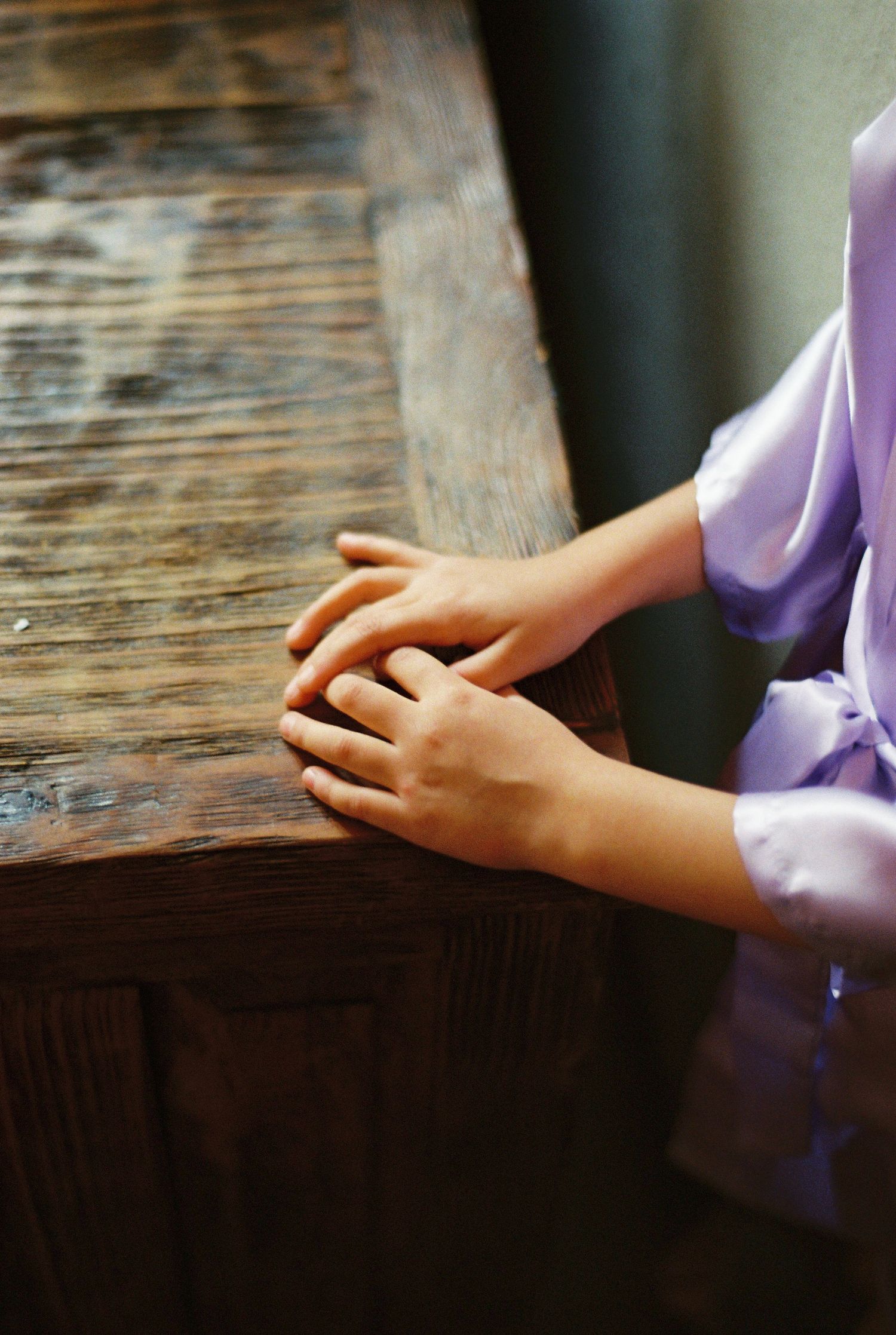 Close-up of hands resting on rustic wooden surface wearing purple sleeve.