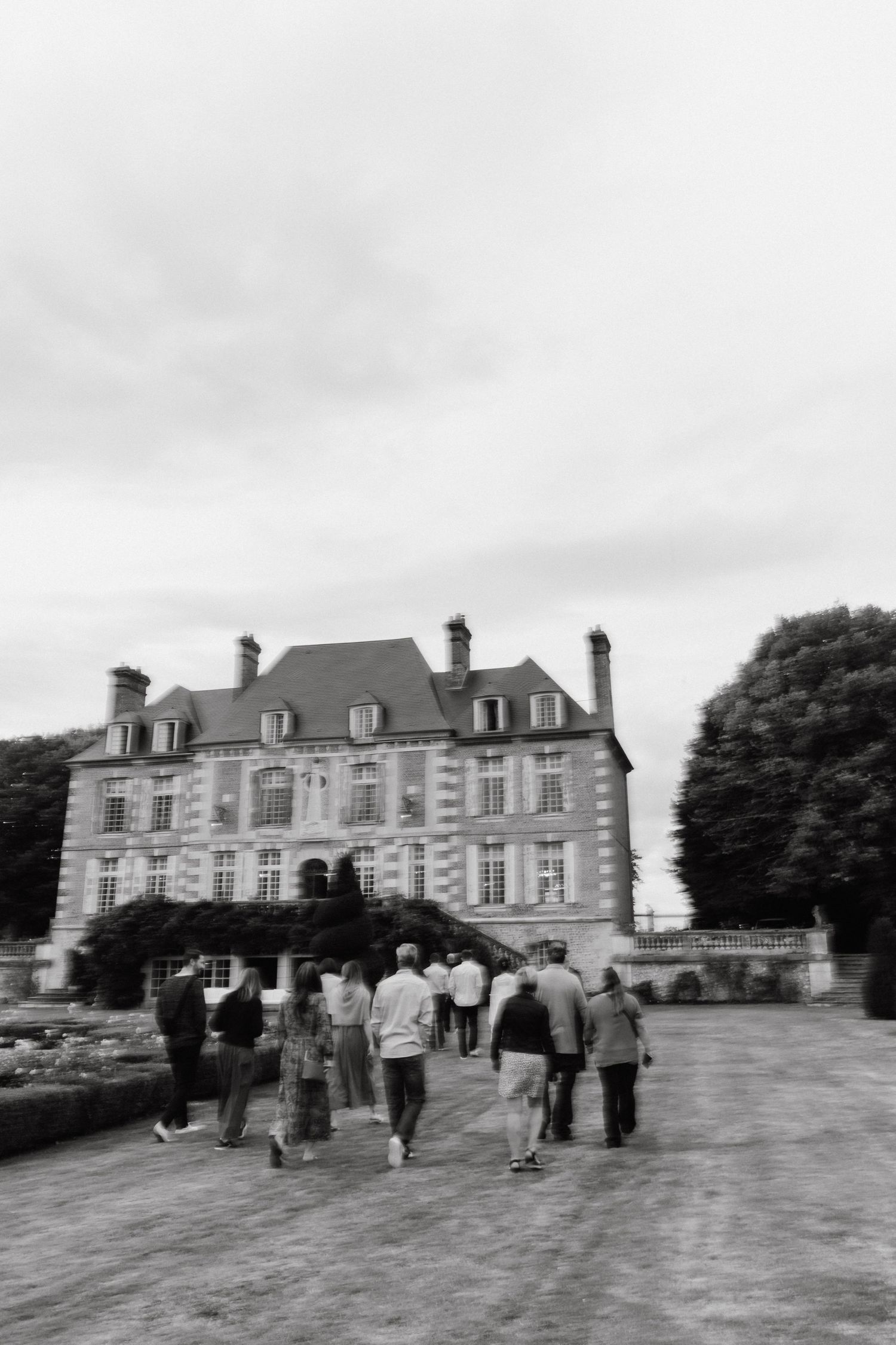 Visitors gather outside a grand French chateau-style mansion with dormers and classic architecture.