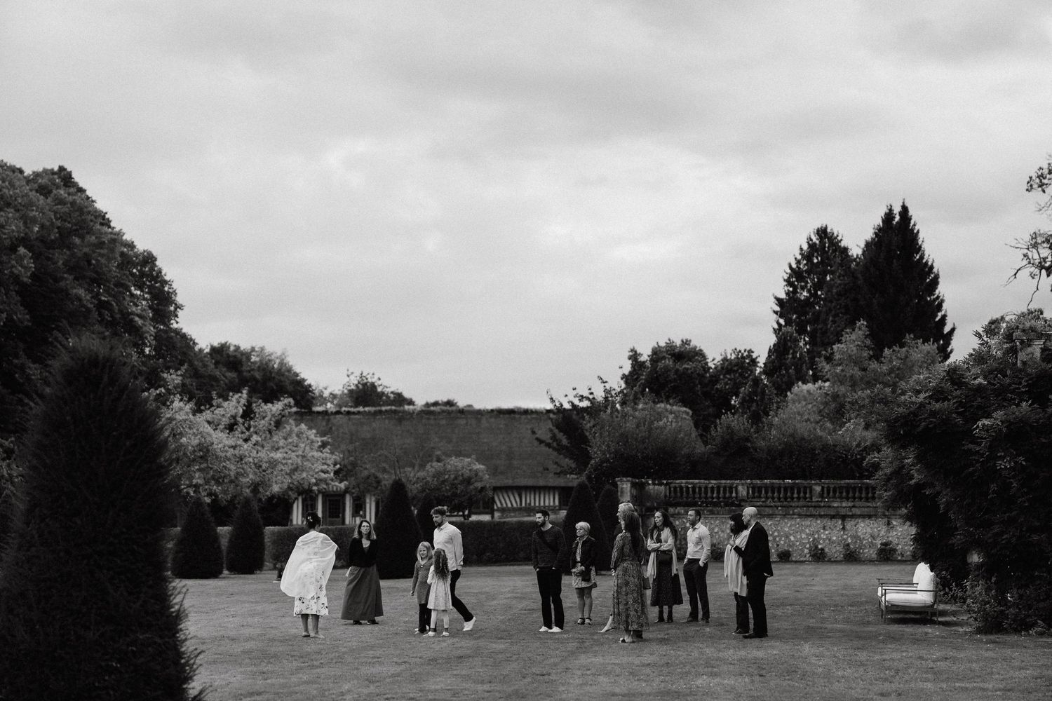 Empty white chairs arranged outdoors on grass for a wedding ceremony.
