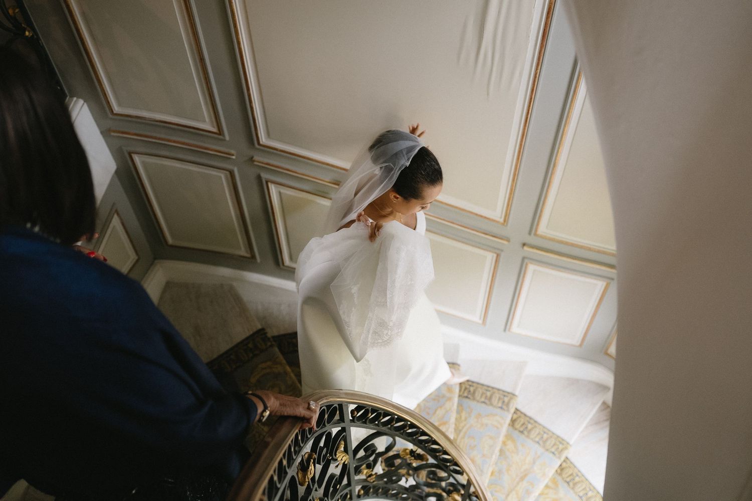 A bride in white descending an elegant spiral staircase in a historic building.