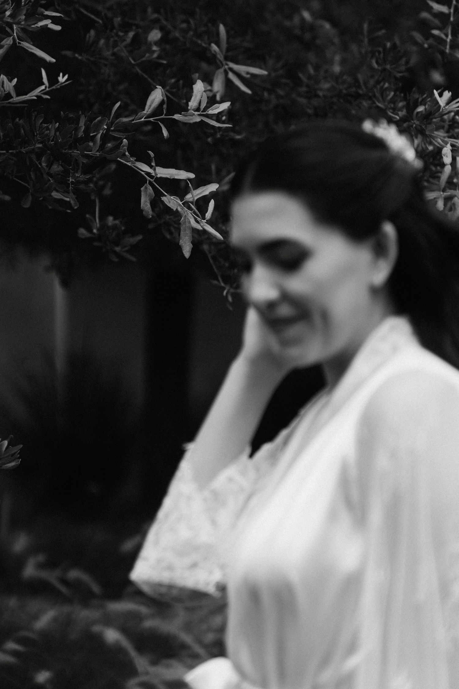 Artistic black and white portrait of someone in a white robe under foliage.