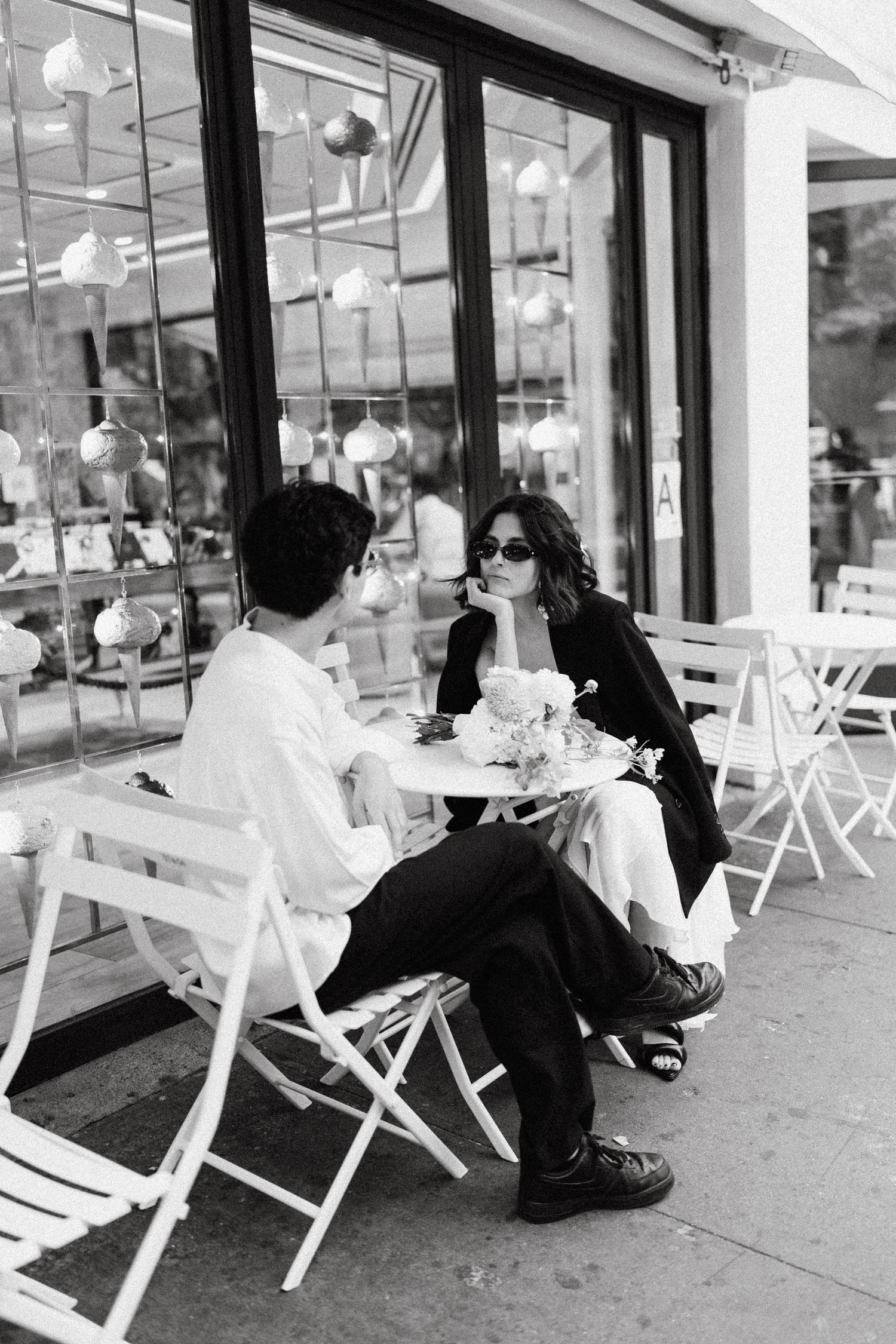 Couple sitting on white folding chairs outside a storefront window.