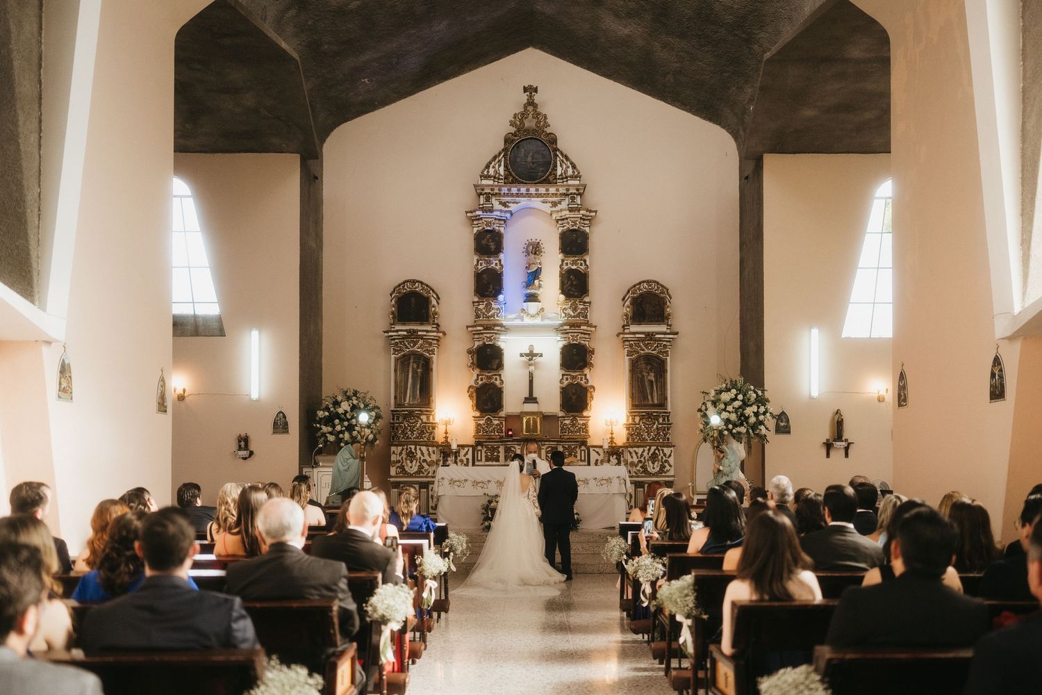 Church sanctuary with white walls and altar decorated with floral arrangements.