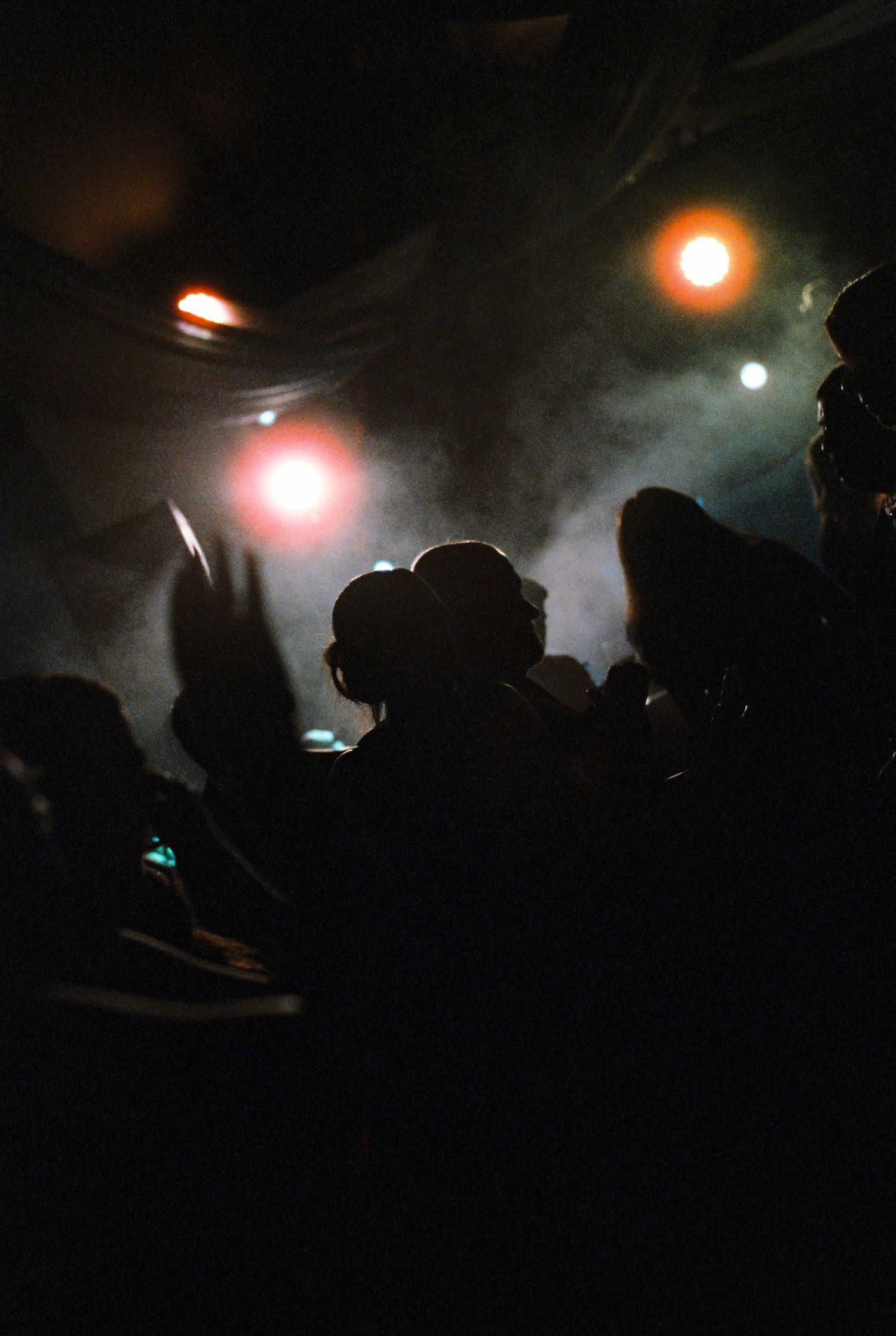 Silhouettes of party guests dancing under colorful lights in smoky atmosphere.