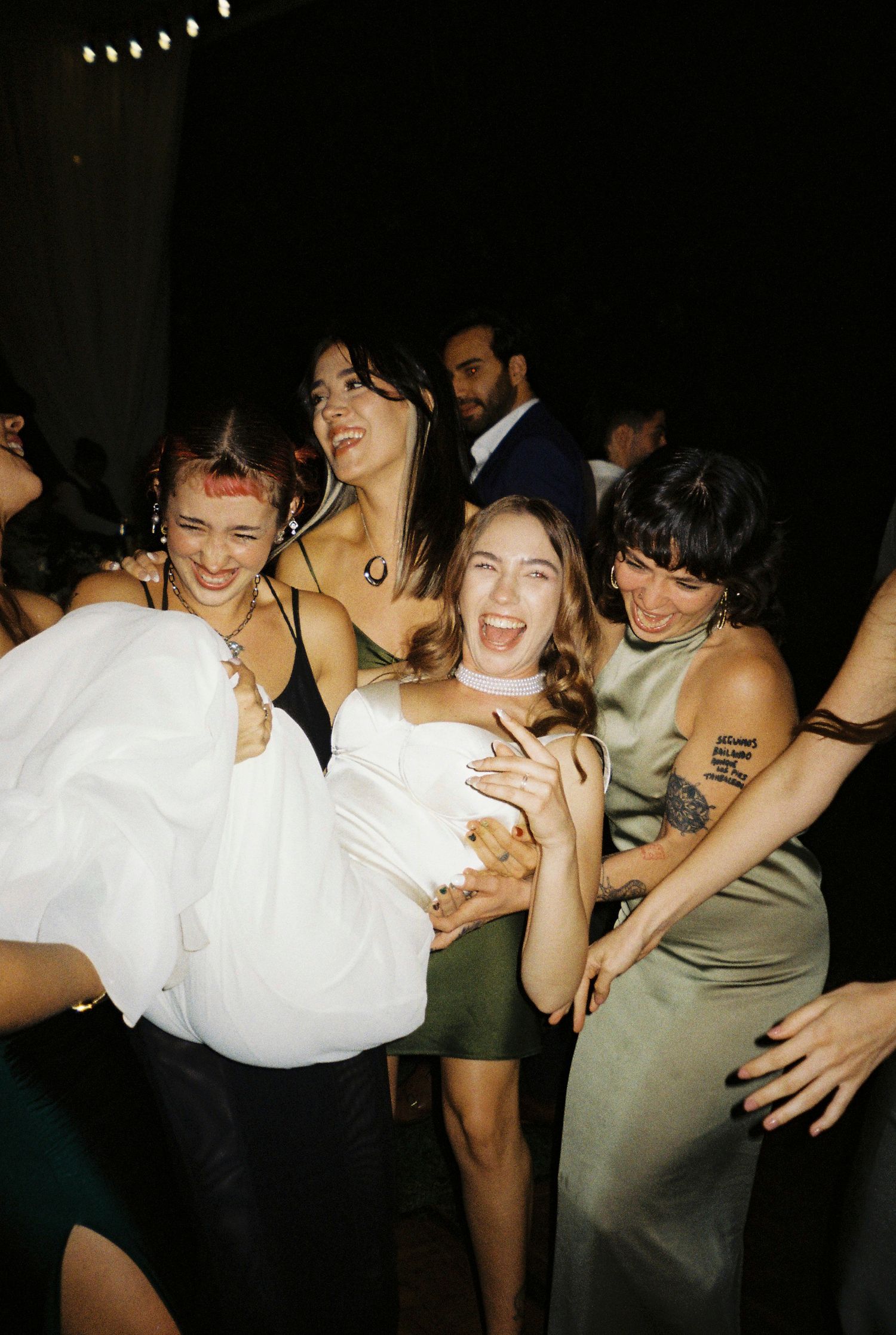Wedding party celebrating and laughing together under string lights at night.