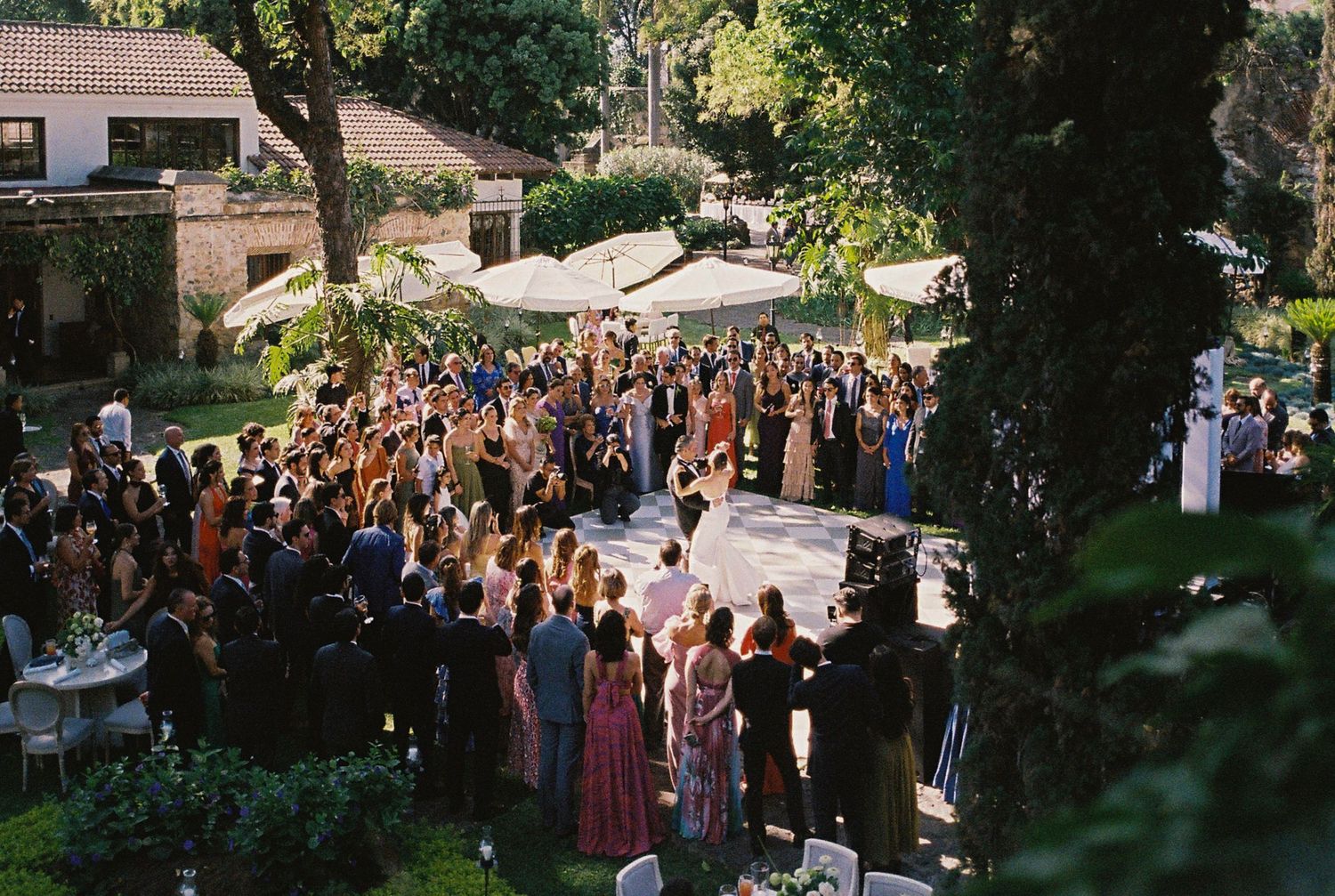 Wedding guests gathered outdoors under tree canopy for ceremony.