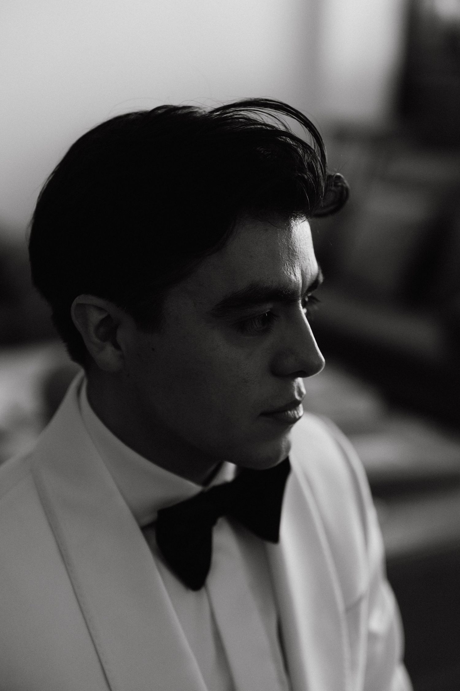A black and white profile view of someone wearing a white jacket in a dark room.