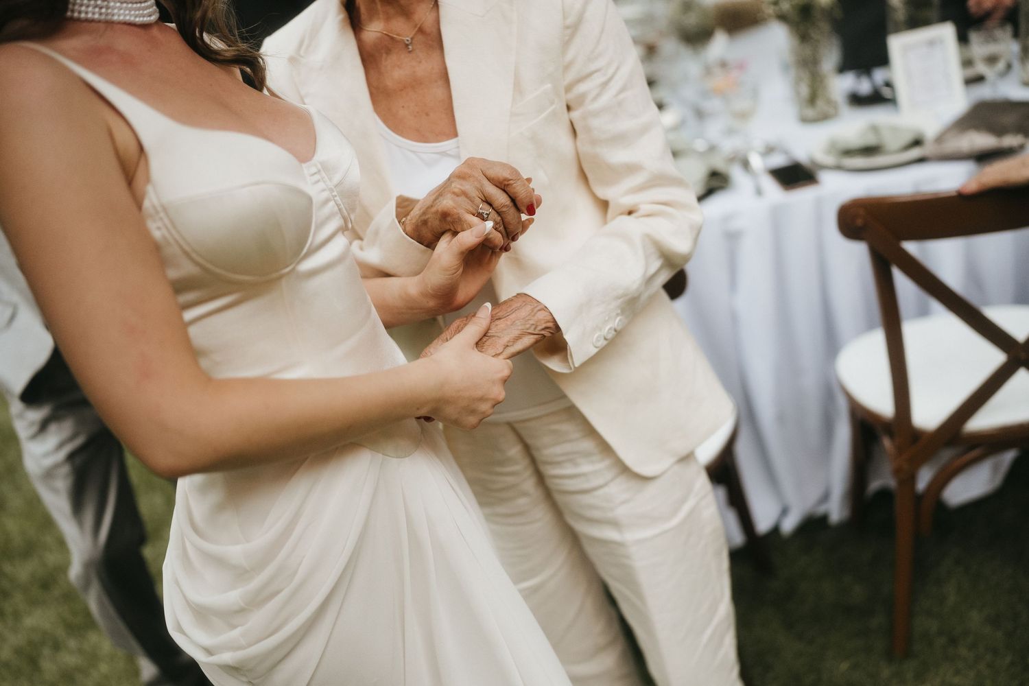 Elegant couple dancing in white and cream formal attire at an outdoor wedding.
