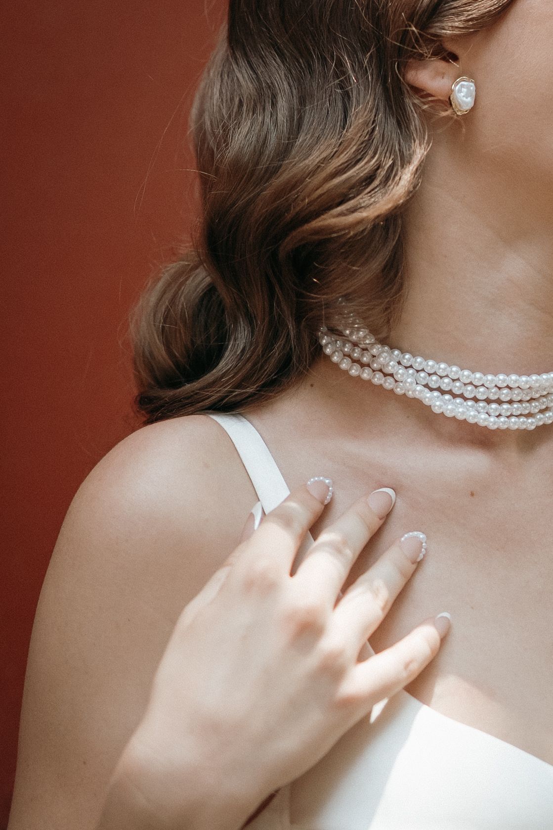Close-up of a pearl necklace and white dress strap in soft natural lighting.