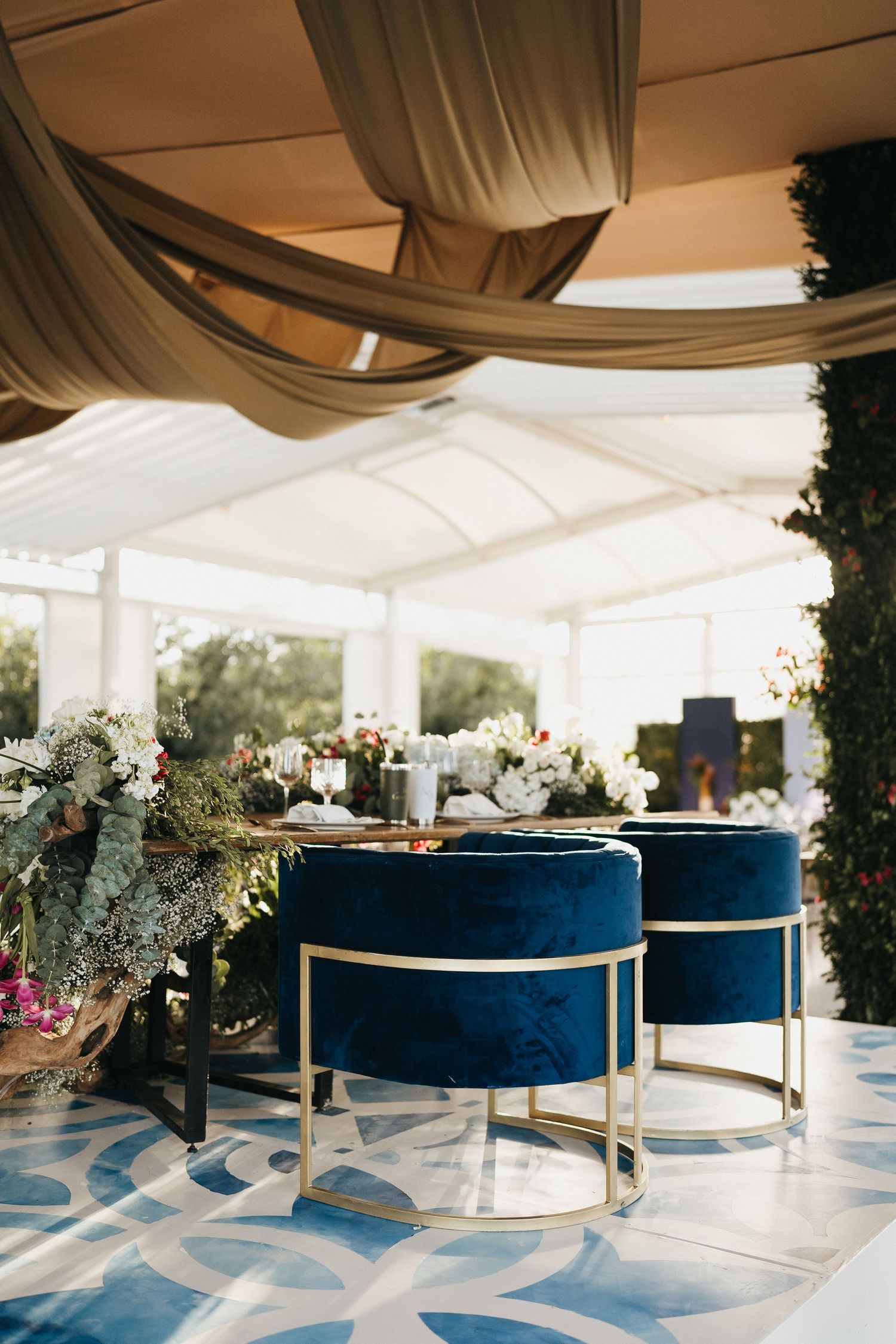 Modern wedding reception setup with blue velvet seating and white tent draping.