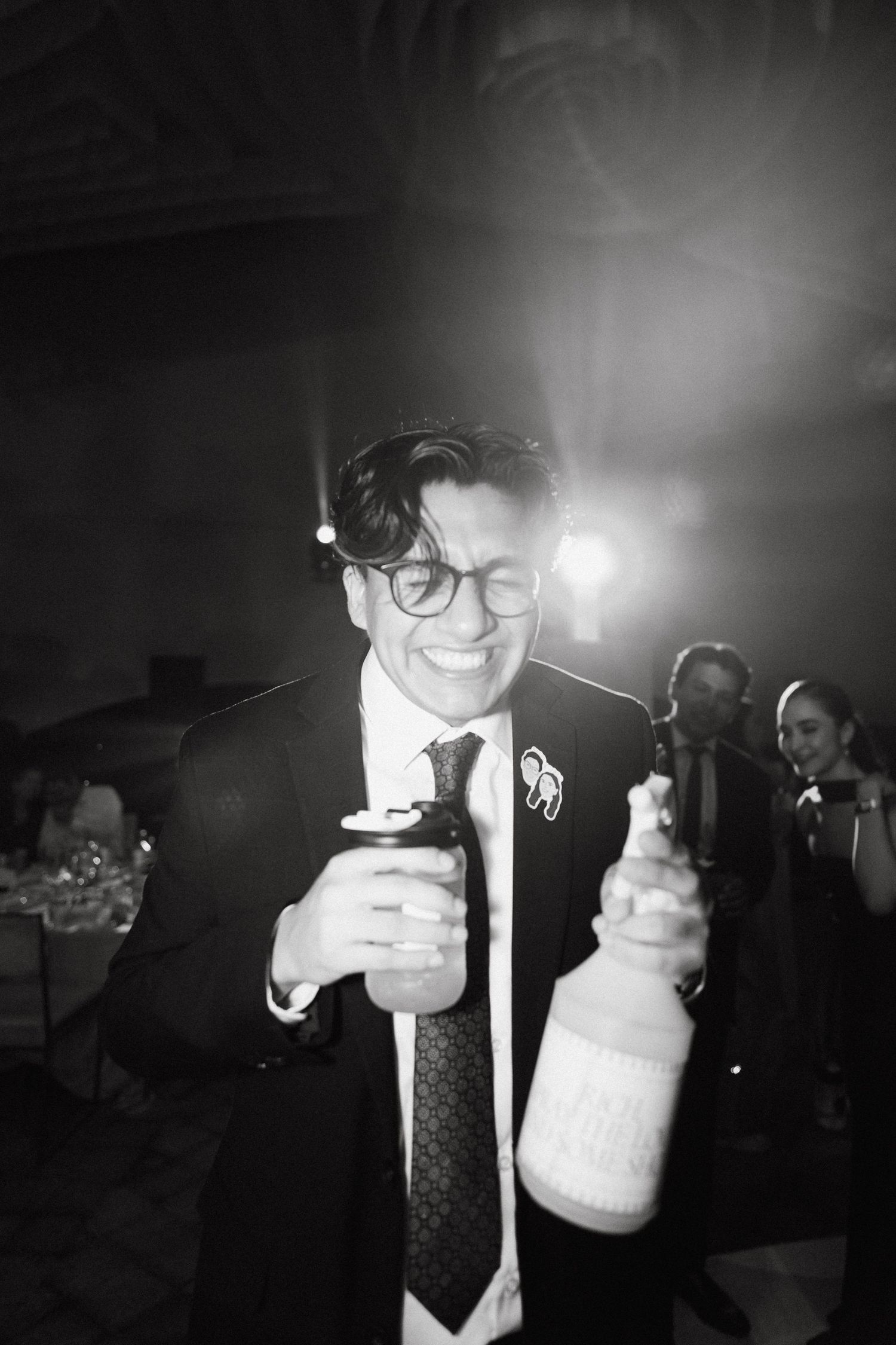 A guest in formalwear holds bottles while celebrating at a dimly lit reception.