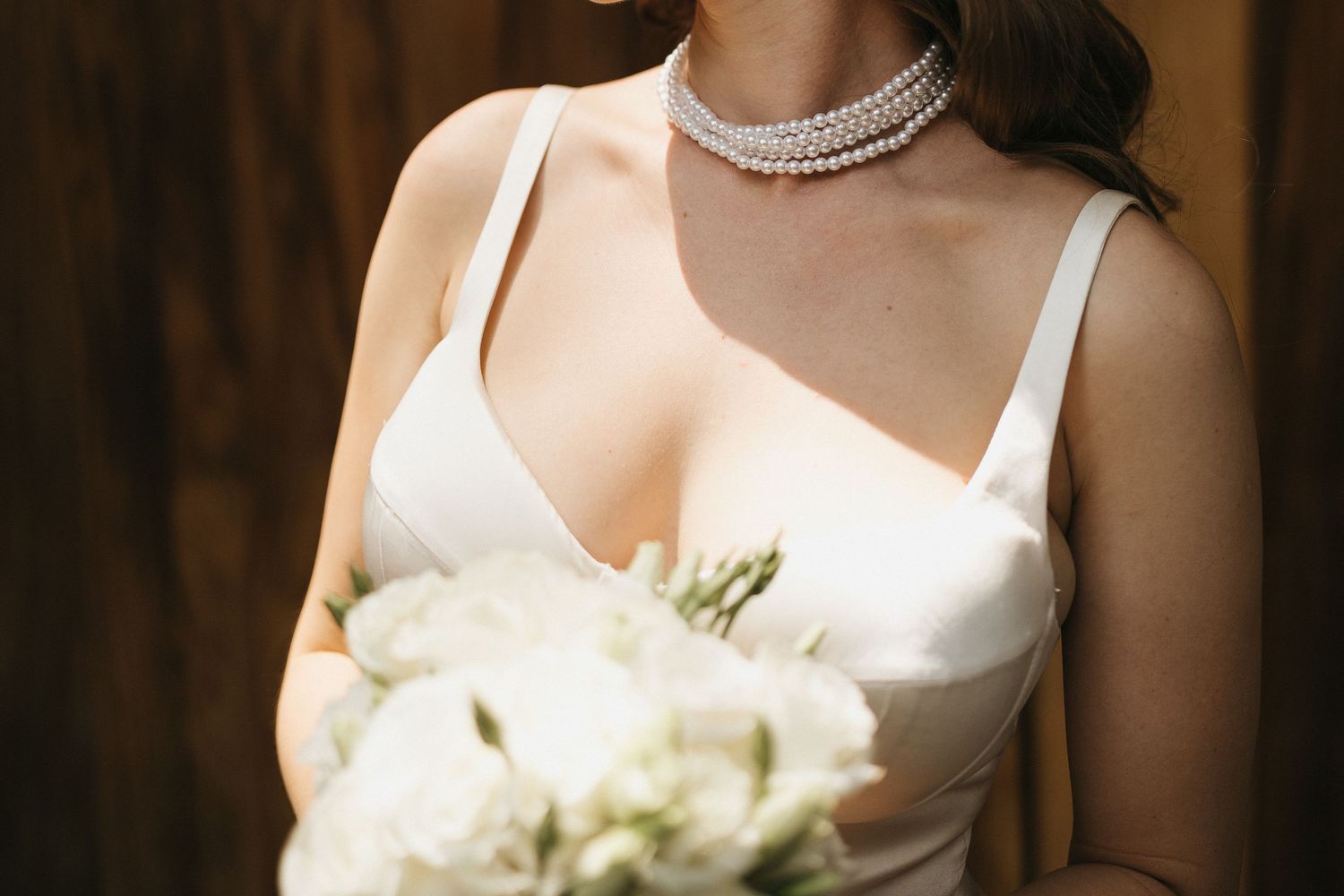 Close-up detail of a pearl necklace and white wedding dress bodice.