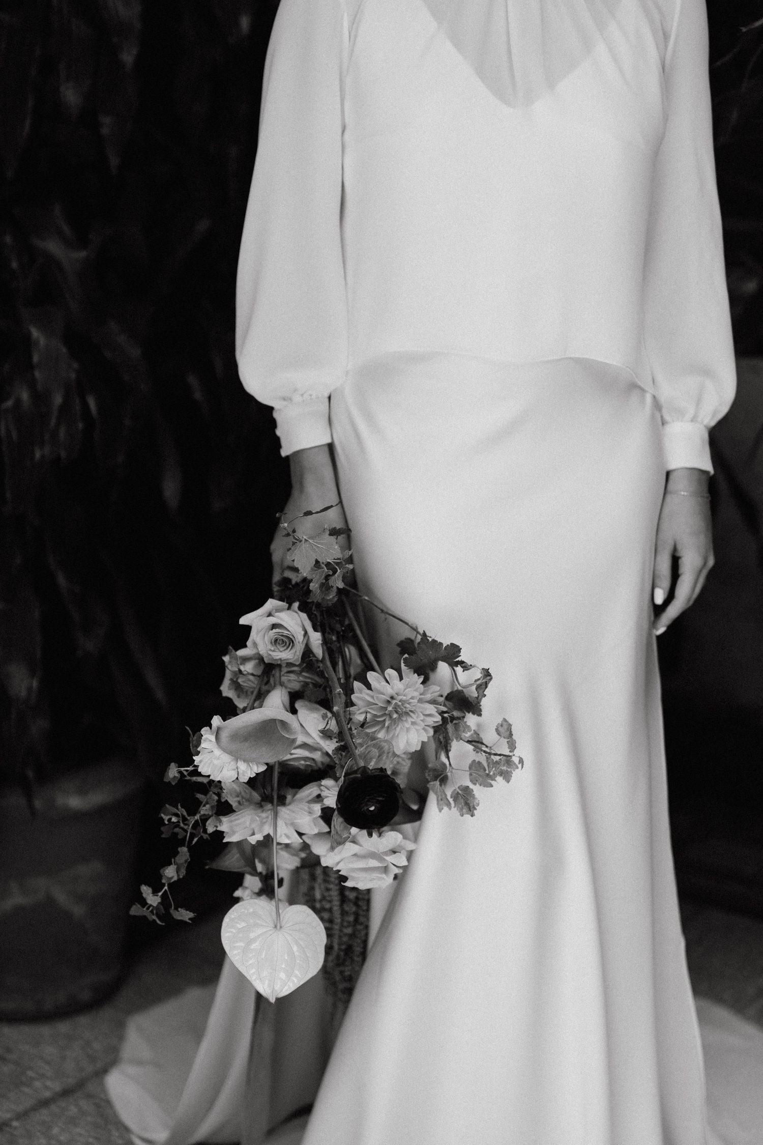 Elegant white wedding dress with flowing sleeves and a delicate floral bouquet.