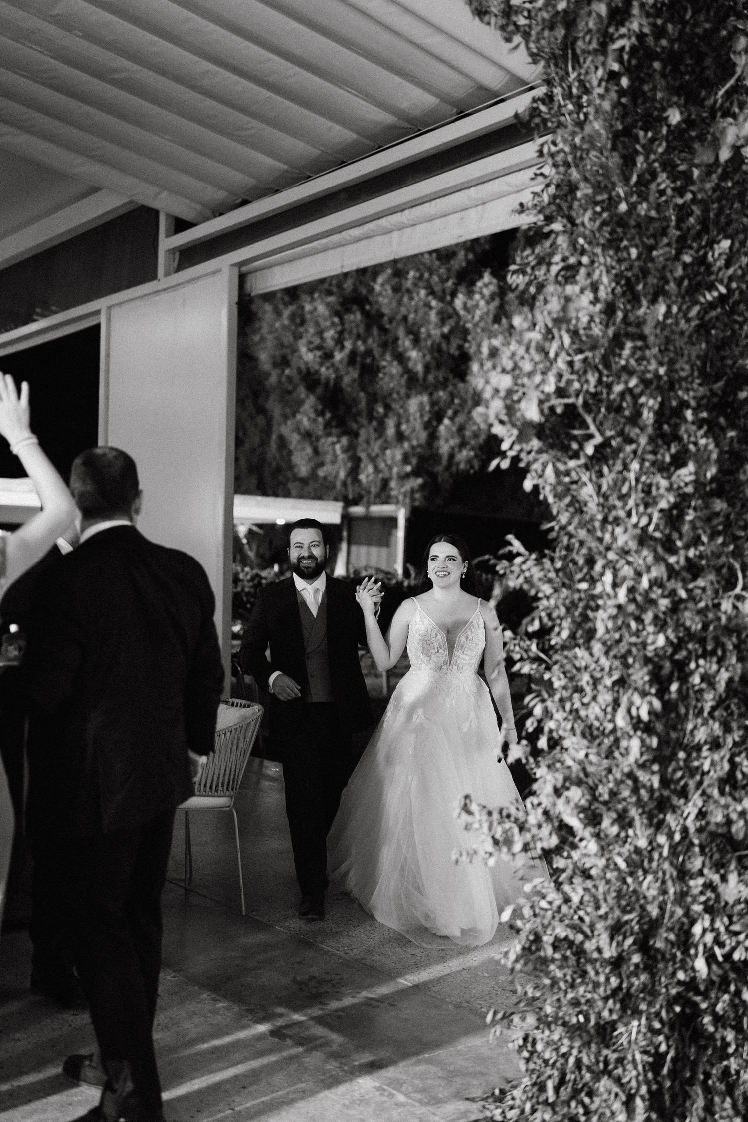 Wedding party entering a venue decorated with greenery and white draping.