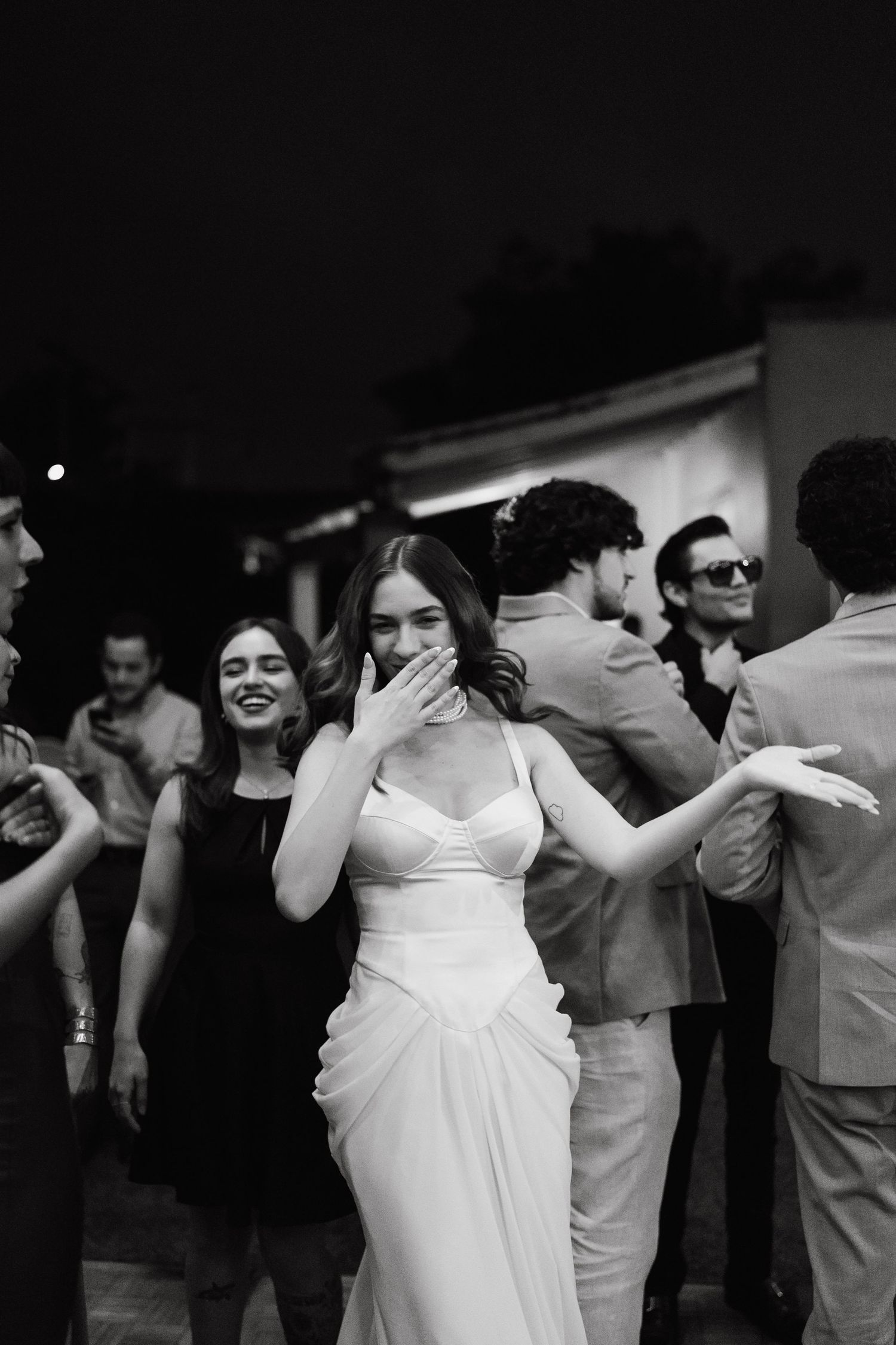 Black and white photo of joyful dancing at a wedding reception with people in white attire.