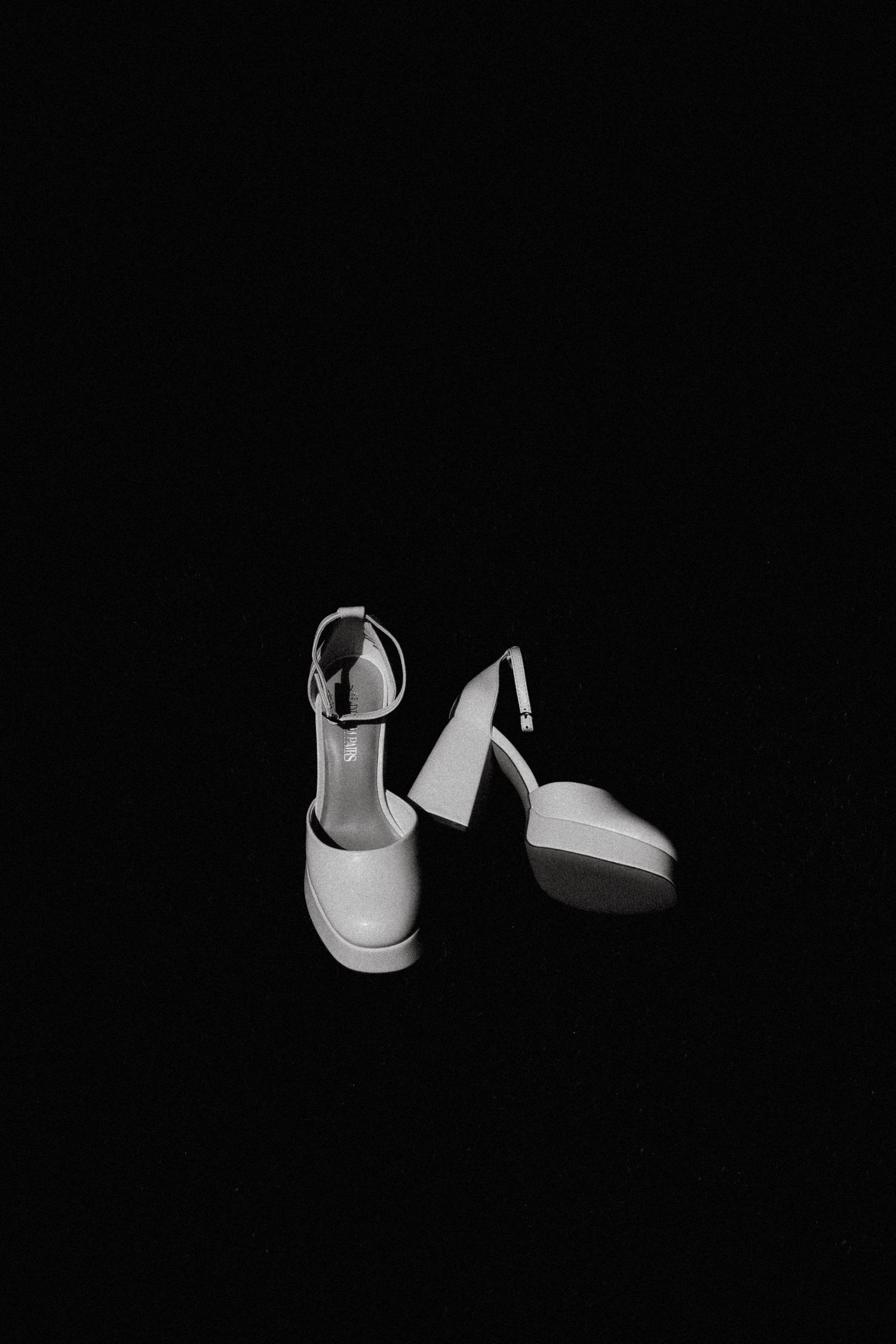 Elegant white bridal shoes displayed against a black background in a minimalist style.