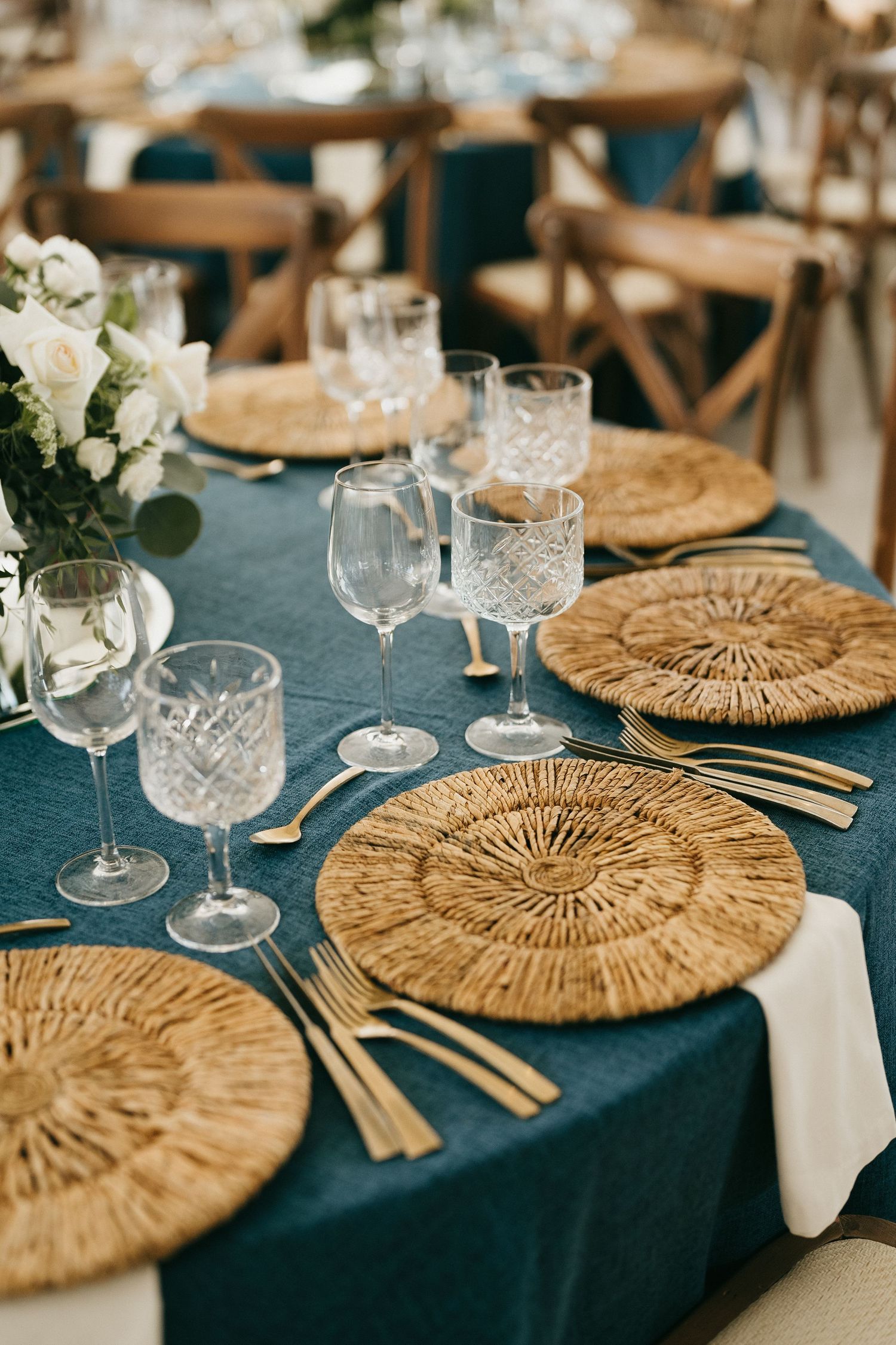 Navy blue tablecloth with woven placemats and crystal glassware at an elegant place setting.
