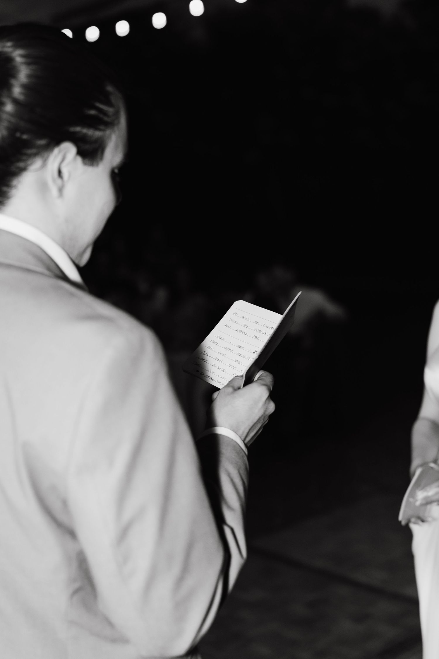 Black and white side profile of figures reading during an evening event.
