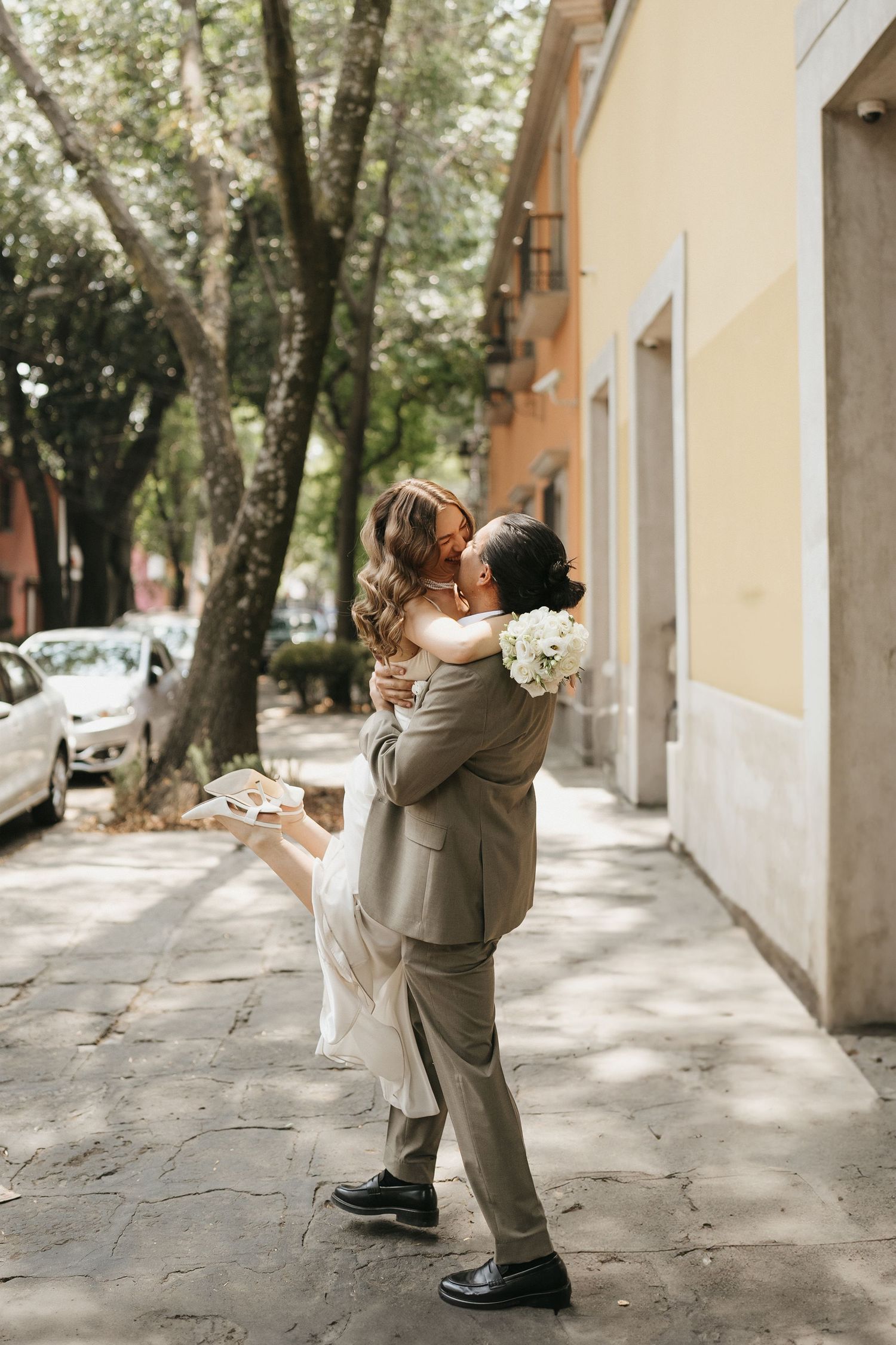 Wedding couple sharing romantic moments on a sunlit city sidewalk.