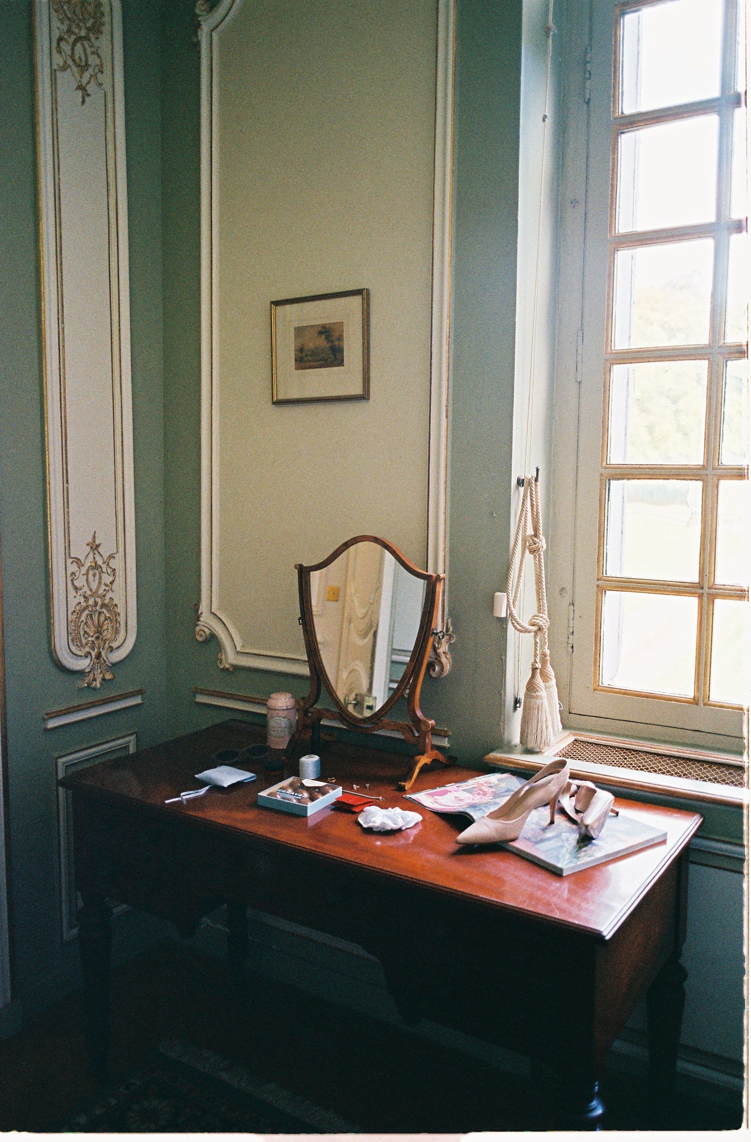 Interior view of an elegant room with mint green walls, tall windows, and antique desks arranged in a row.