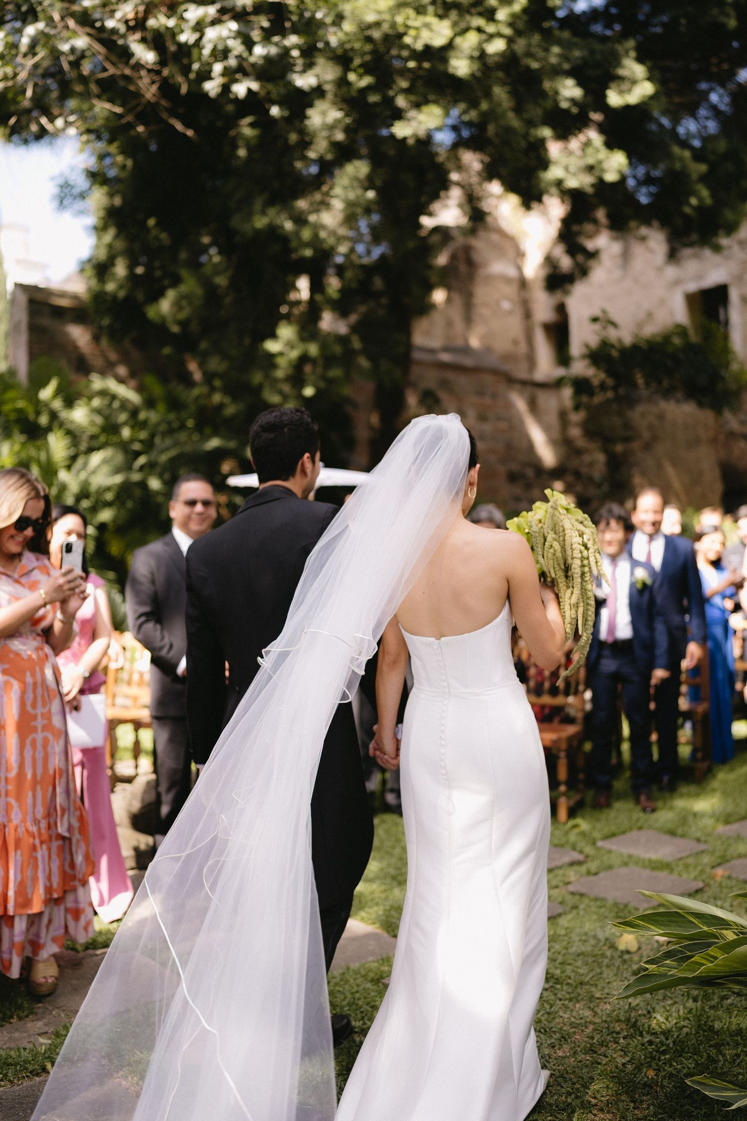 Elegant outdoor wedding ceremony with guests watching a couple in a flowing white dress and veil.